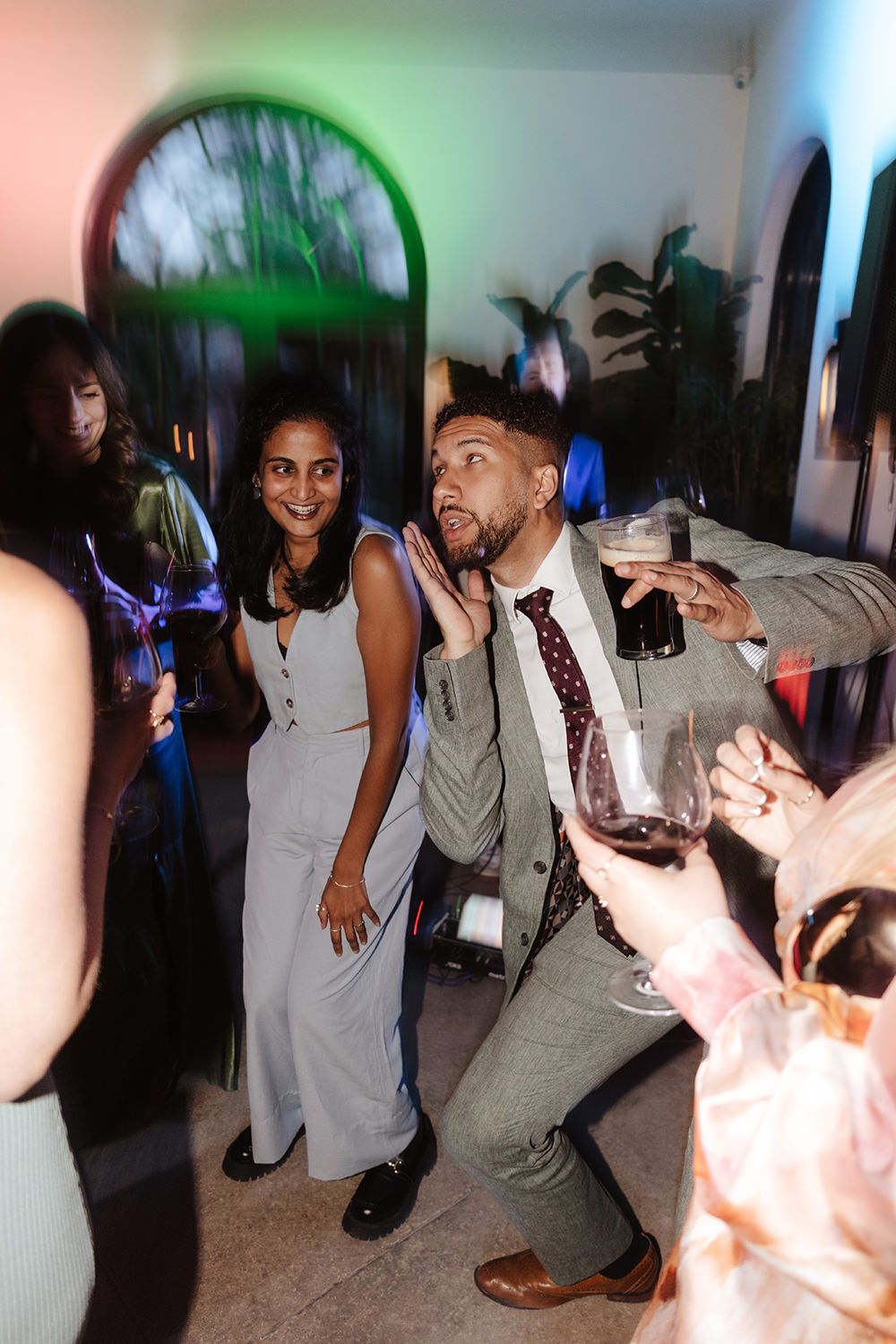 Party guests dancing and having fun at a celebration with colorful lighting and arched doorways in the background.