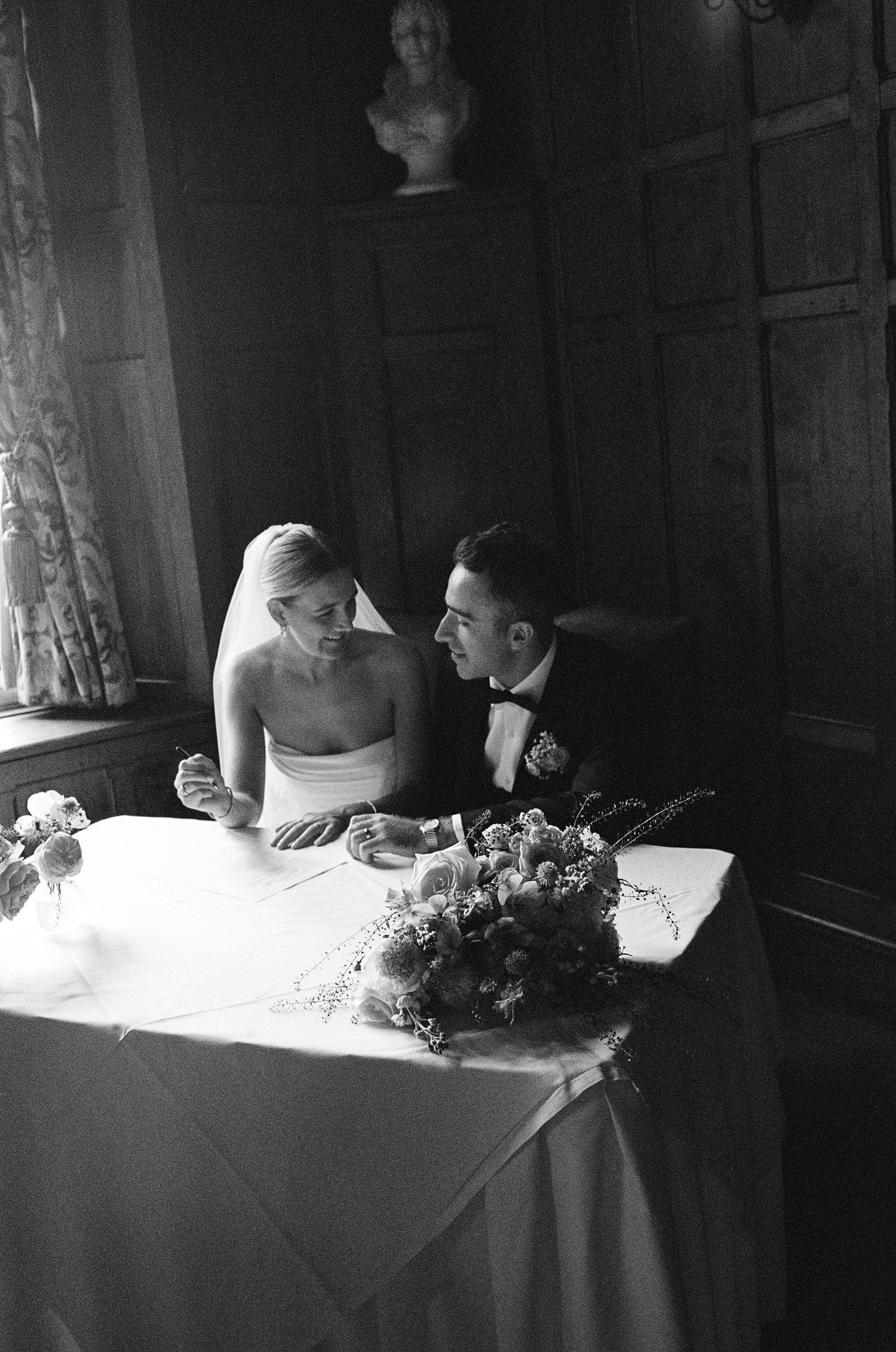 Black and white photo of bride and groom sitting together at a table during their wedding reception.