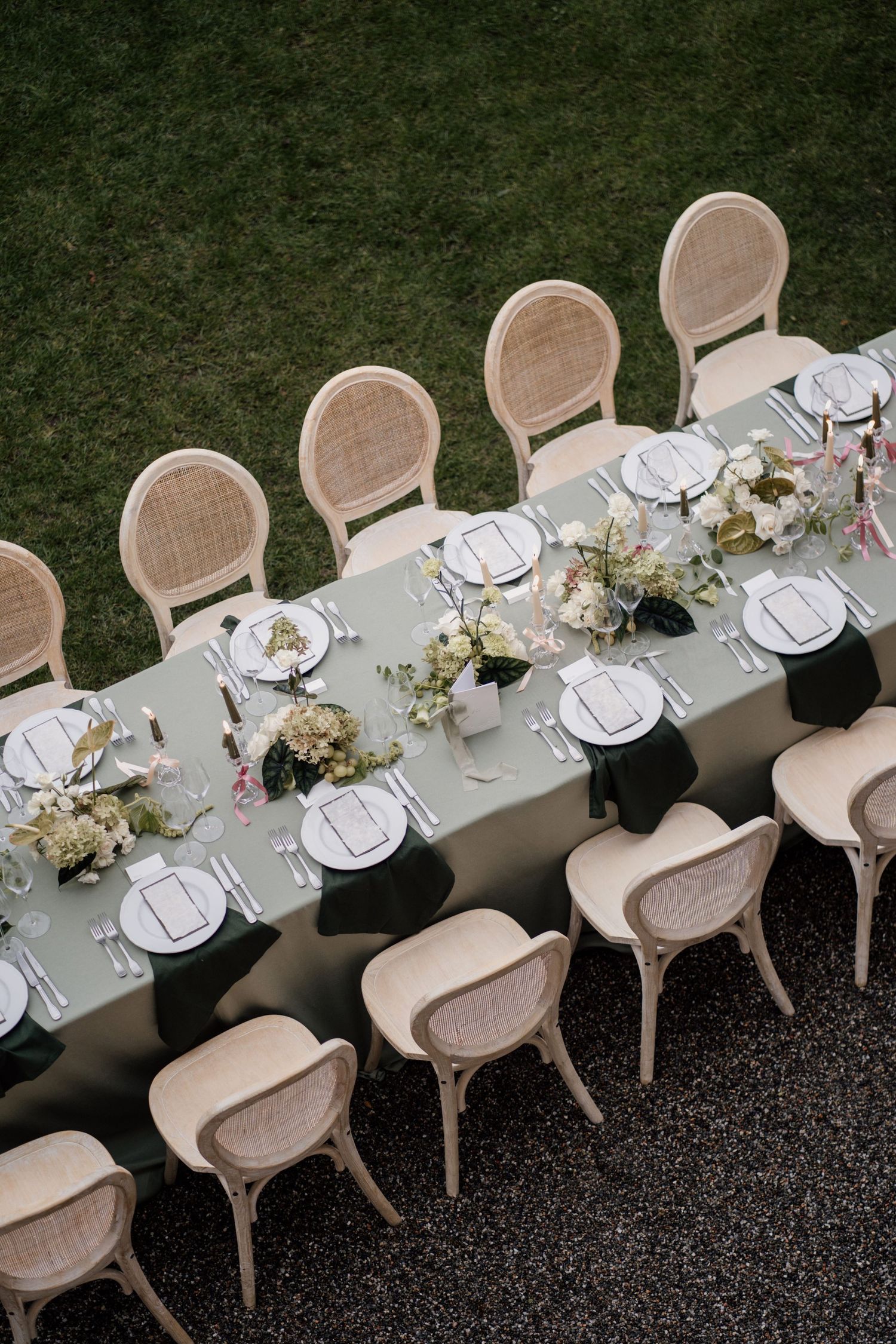 Aerial view of outdoor wedding reception table with rattan chairs and white floral centerpieces.