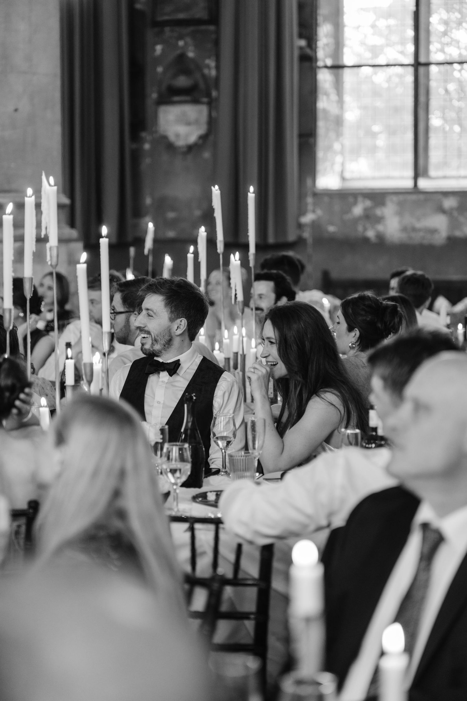 Black and white wedding reception photo with guests seated at candlelit tables in an elegant venue.