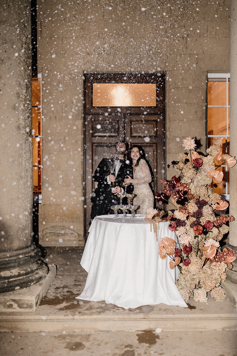 Bride and groom having a champagne spray while standing behind their champagne tower styled with autumnal flowers at Rise Hall.