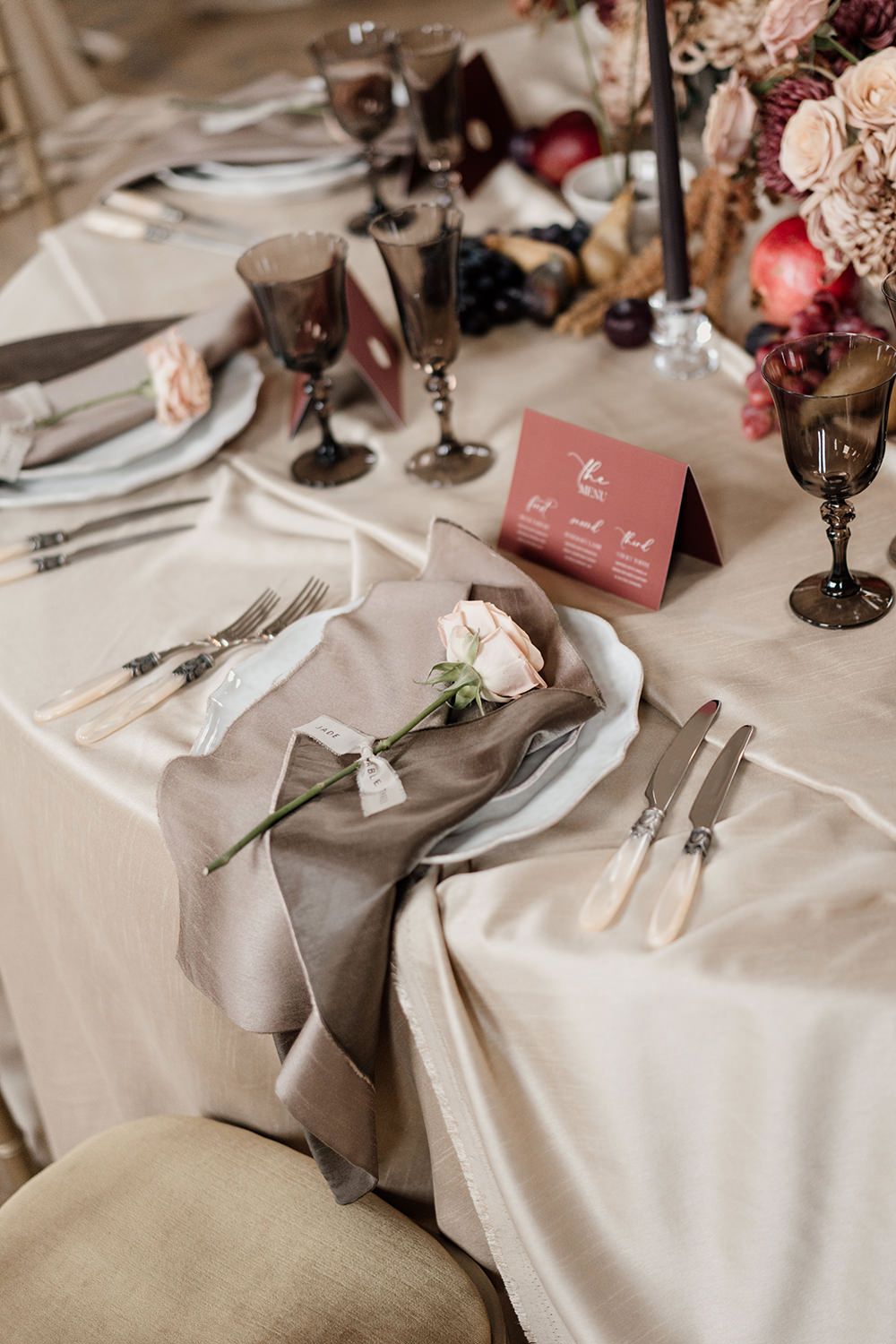 Wedding reception table detail featuring autumnal fabrics, red and burgundy flowers and candles.