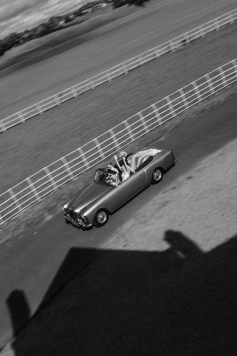 Black and white sequence of a vintage racing car speeding along a curved racetrack, captured from an elevated angle.
