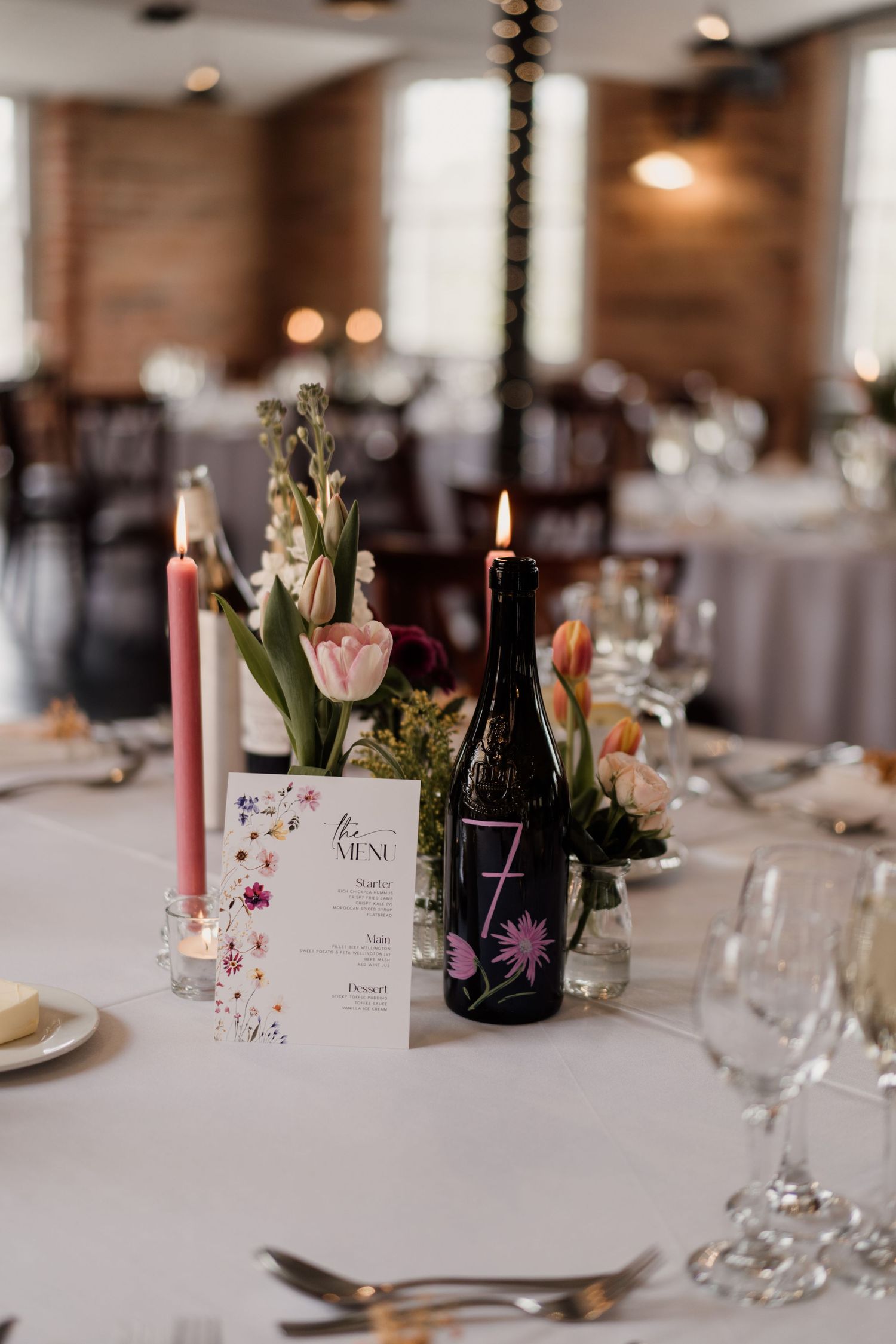 Wedding table centerpiece with floral menu card, pink candles and wine bottle.