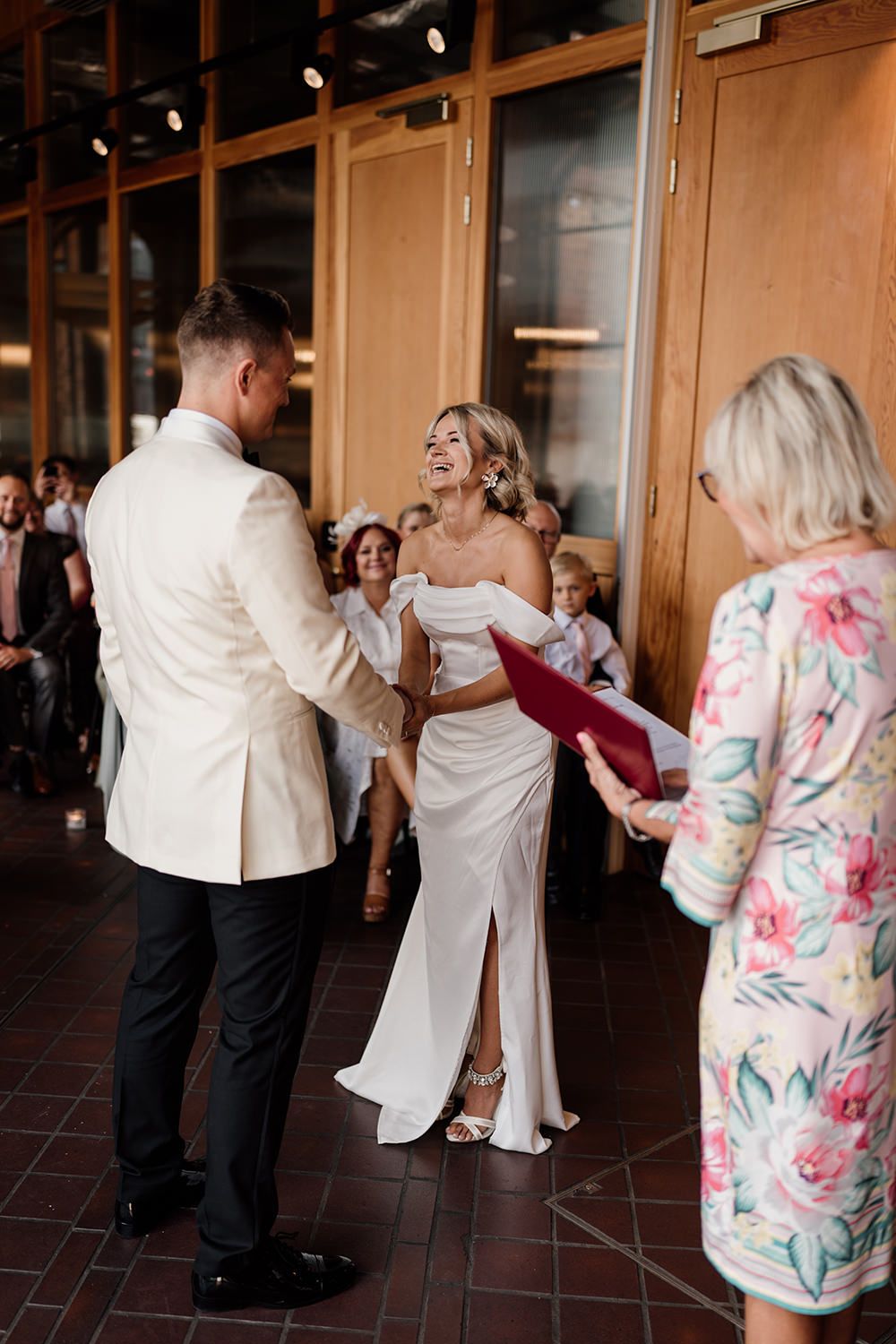 Wedding ceremony celebration with guests gathered in an indoor venue with warm lighting and hardwood floors.