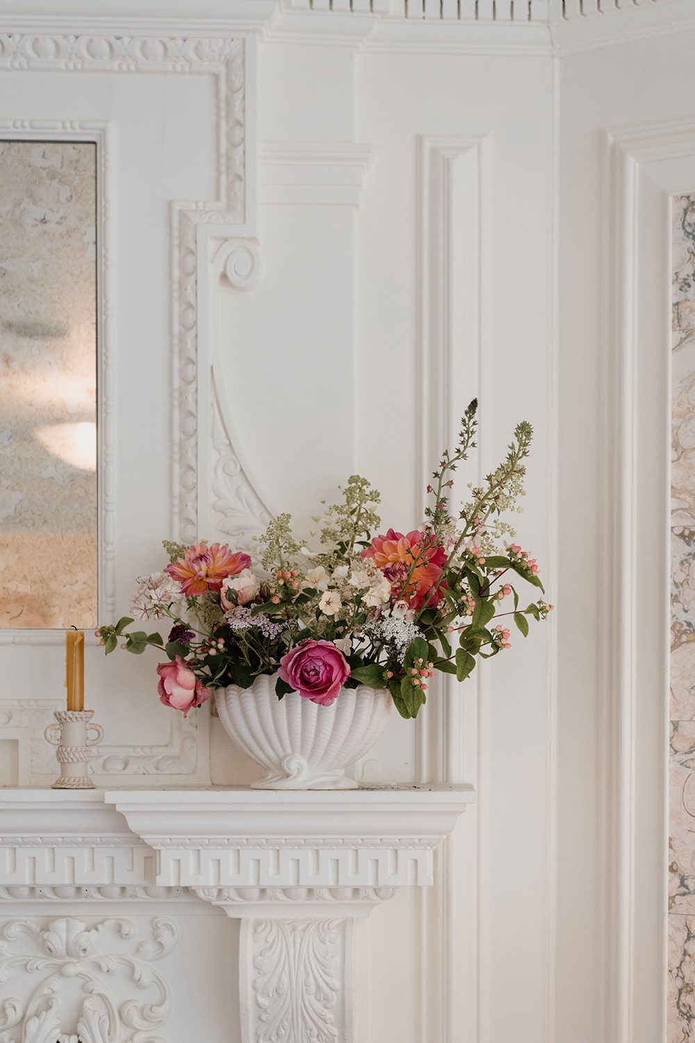 Colourful flowers arranged in a white vase on a white fireplace at the reception room in Kin House.