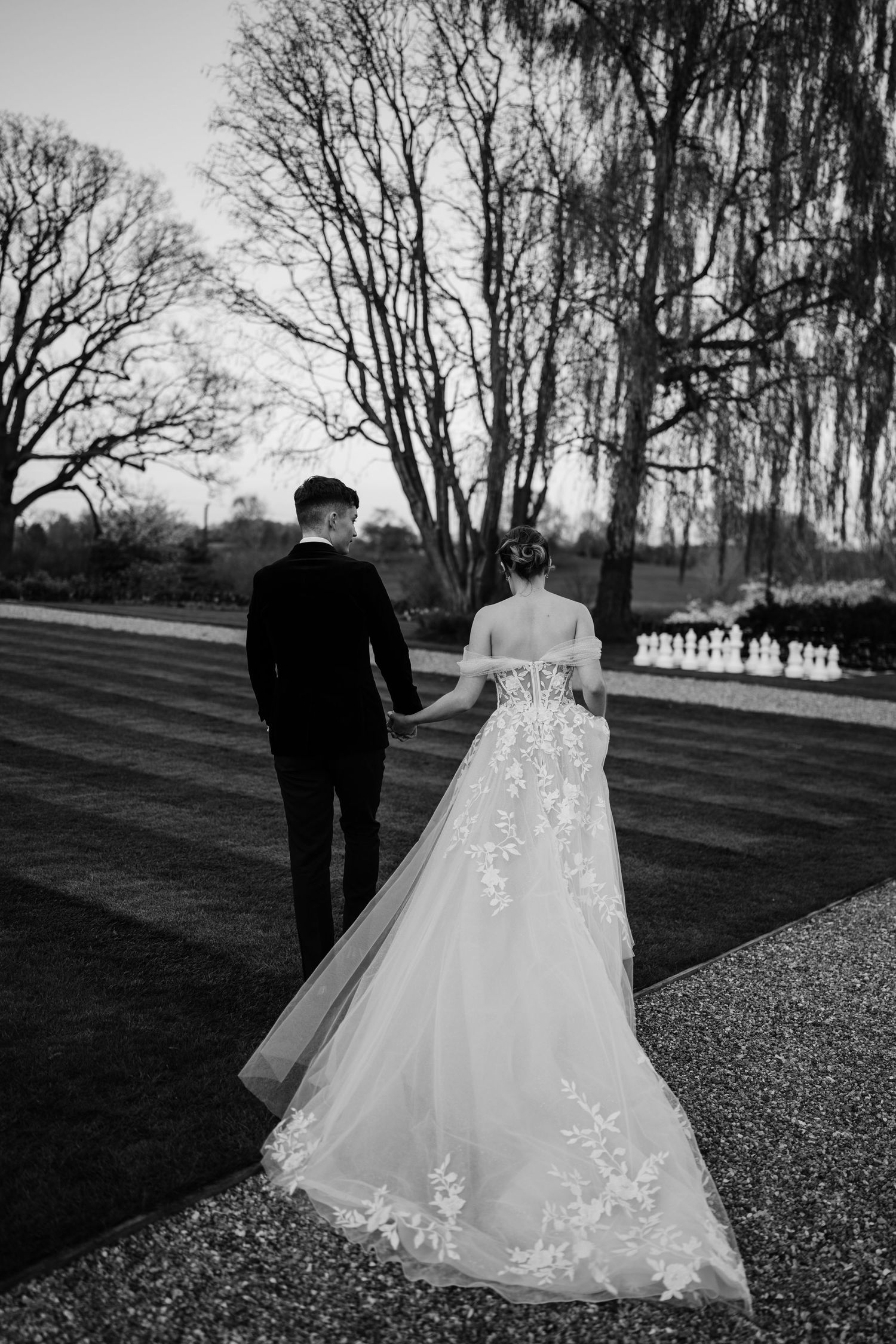 Bride and groom holding hands, walking away from the camera in the grounds of Bourton Hall.