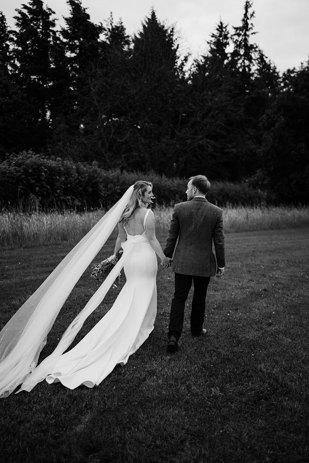 Bride and groom holding hands walking away from the camera in the grounds of the hovels harewood.