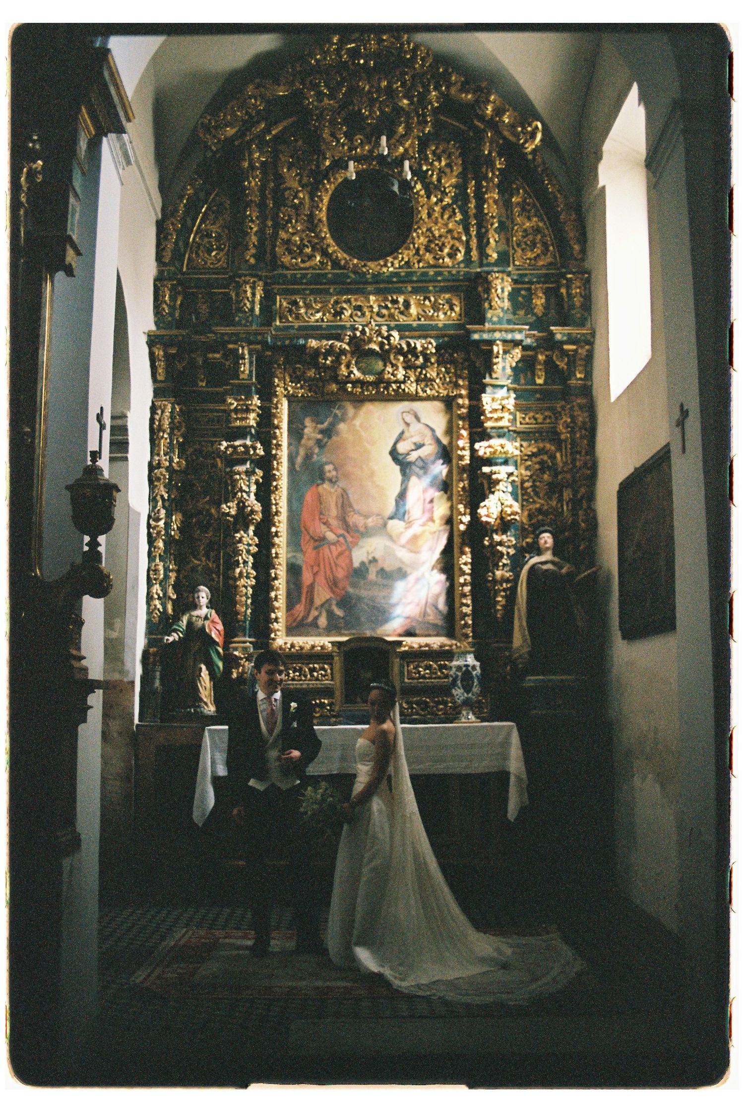 Bride and groom stand before an ornate gilded baroque altar during their wedding ceremony in a historic chapel.