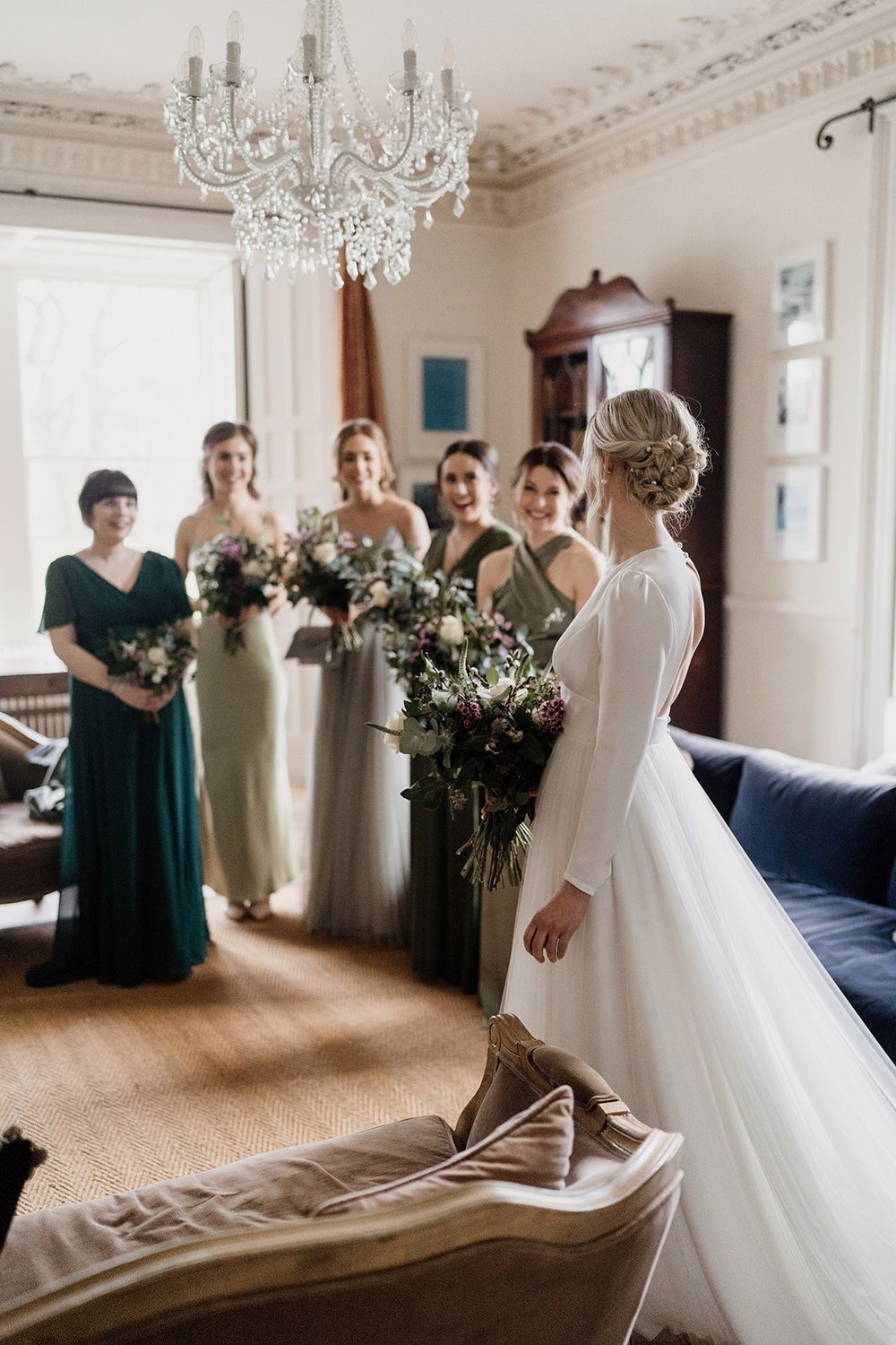 Bride facing away from camera looking at her bridesmaids who are wearing green dresses.