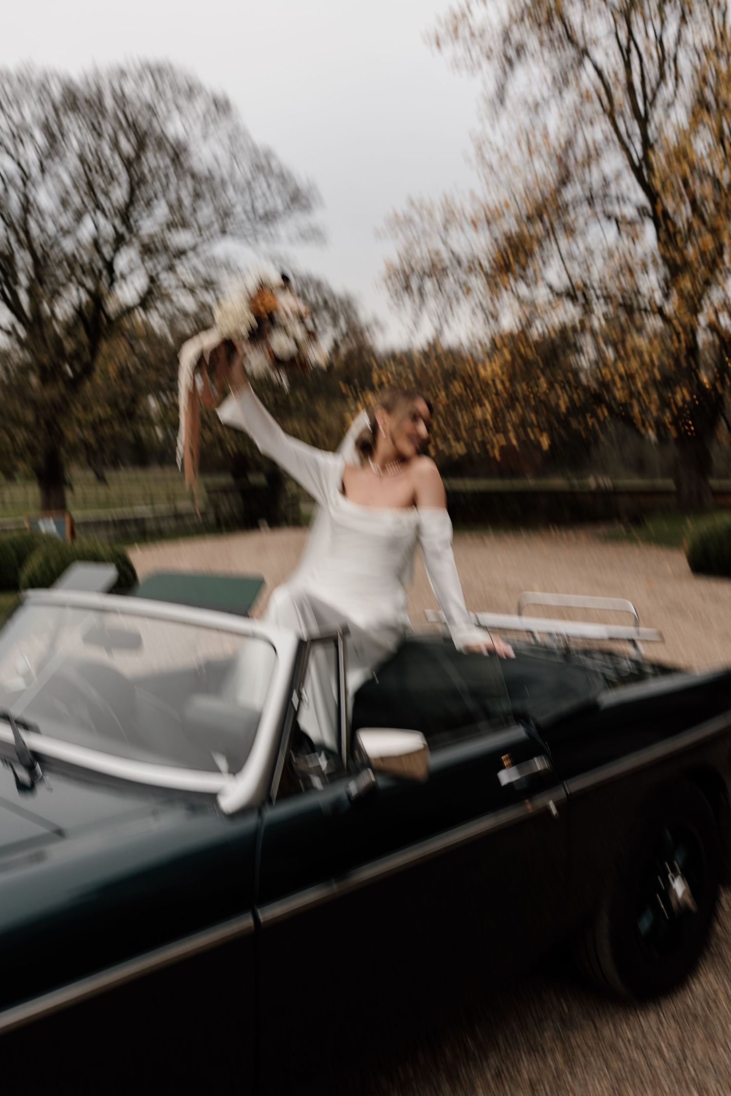 Black vintage convertible car parked in autumn setting with white fabric flowing in the breeze.