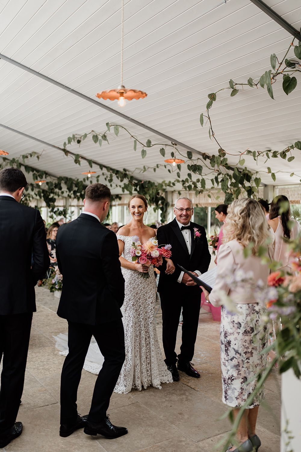 Bride smiling at her husband to be as she walks down the aisle with her father.