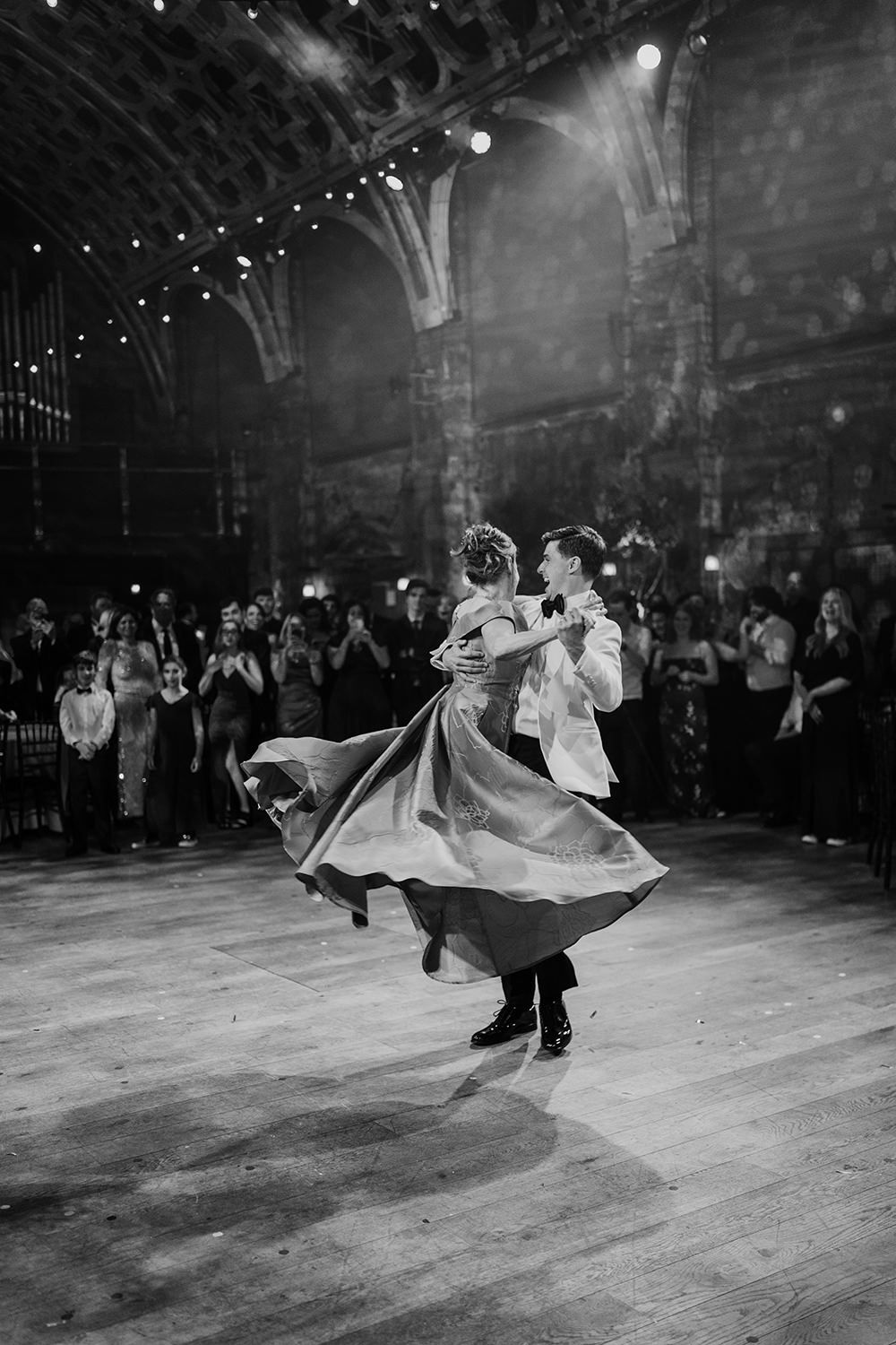Groom dancing with his mother during their first dance, she's in the air as her dress flows and people watch.