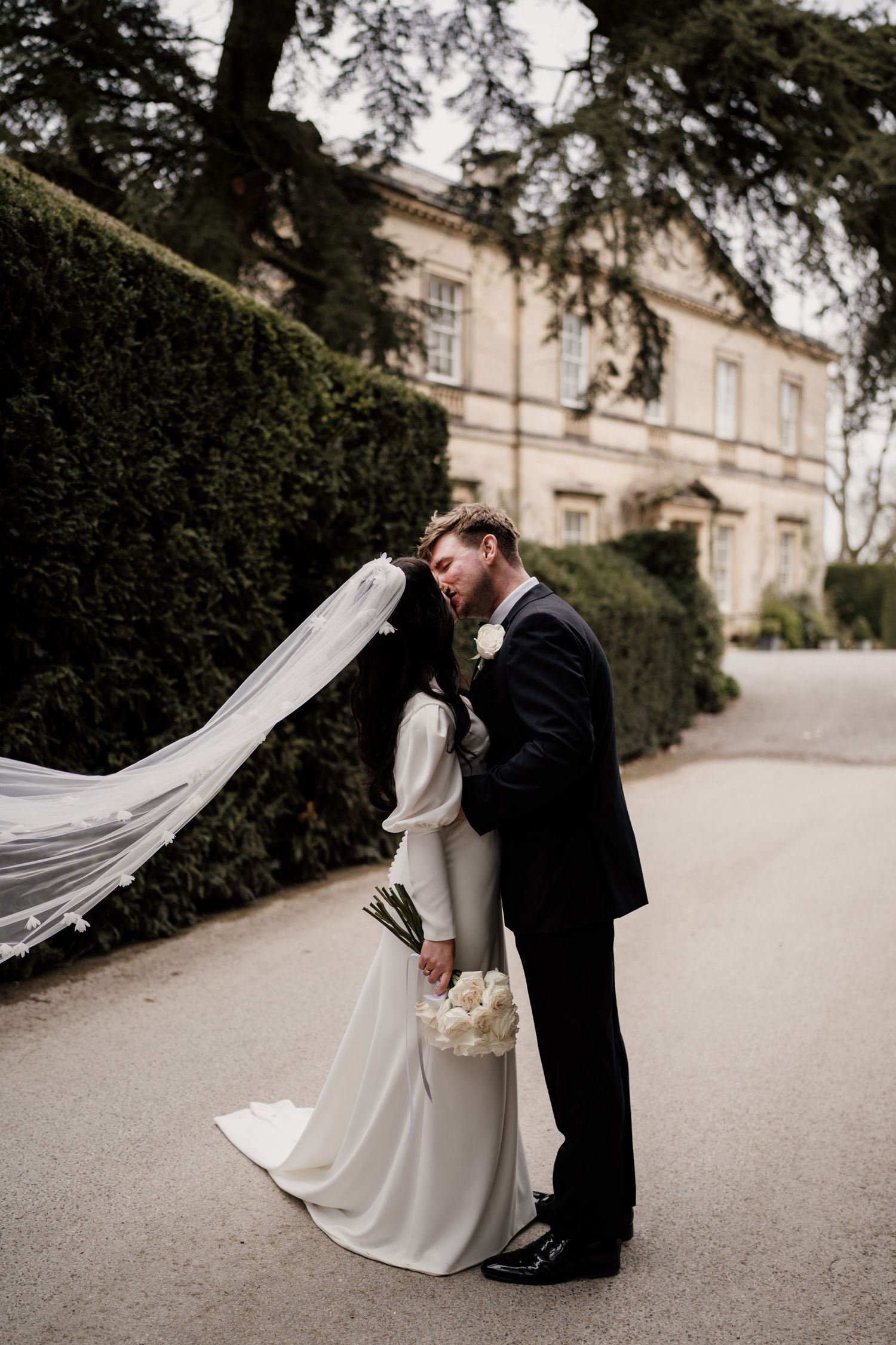 Bride and groom kissing as the brides veil catches the wind at Middleton Lodge Estate.