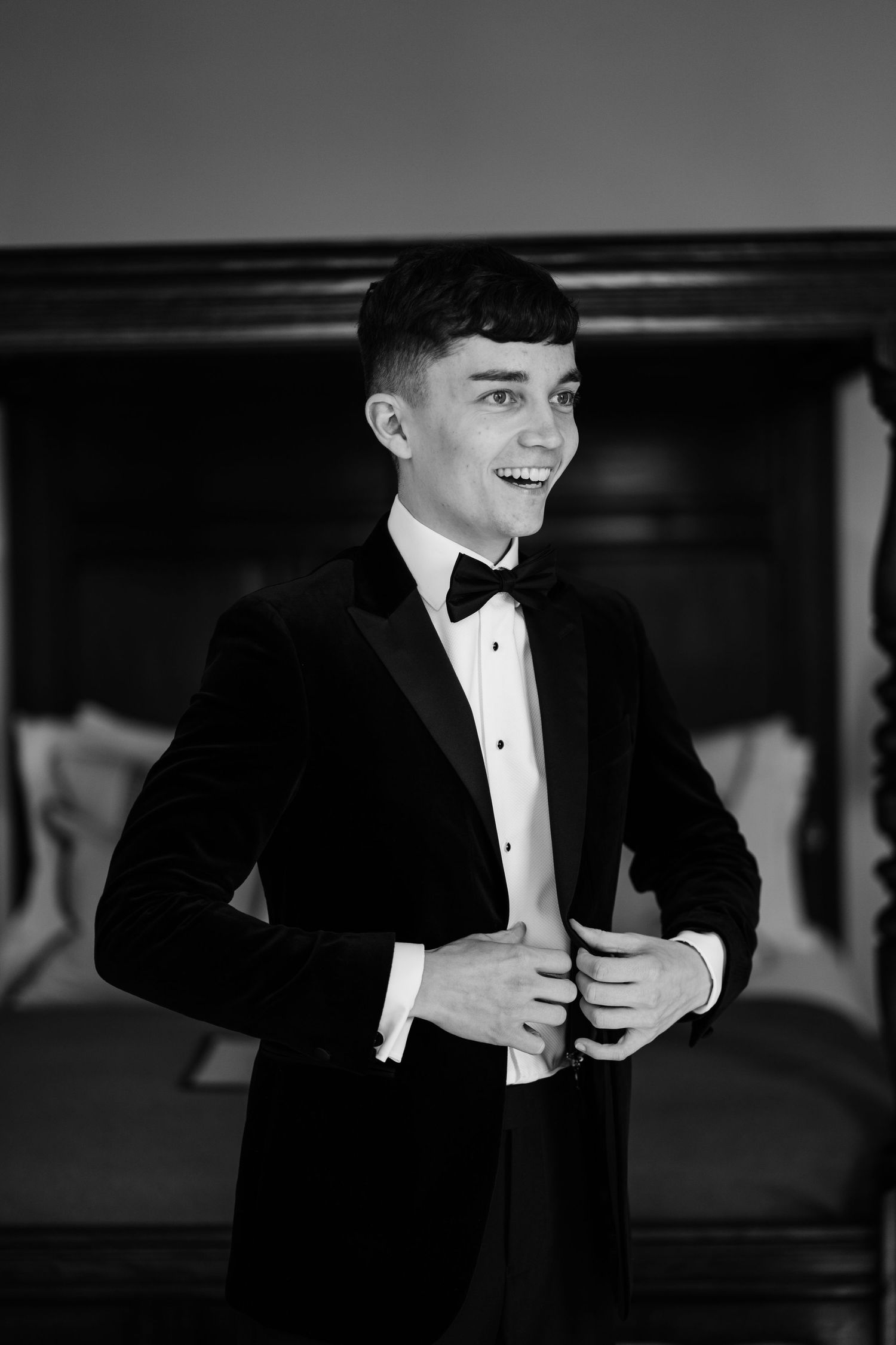 Groom fastening his blazer while smiling.