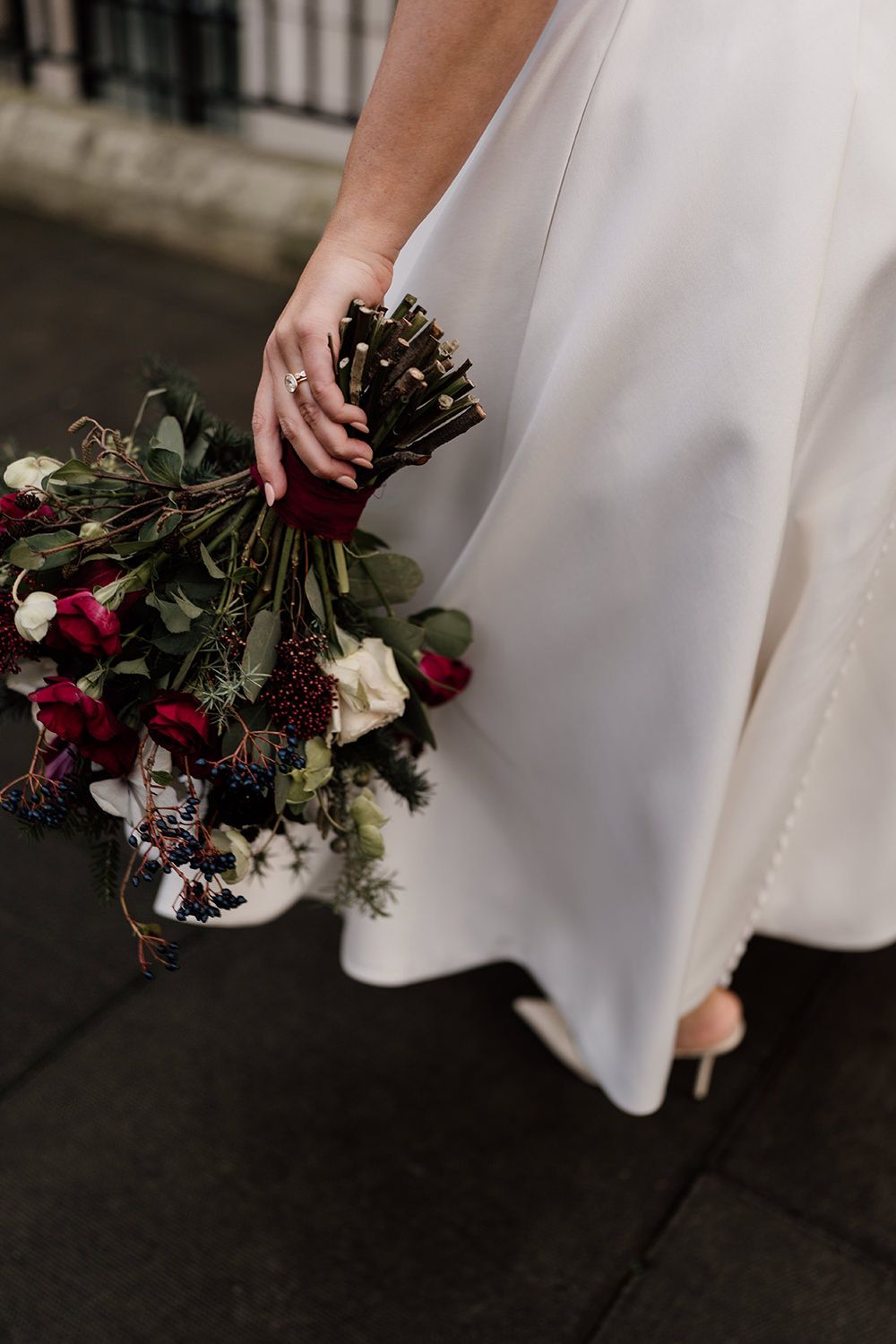 Close-up details of white wedding dress with burgundy and white floral bouquet highlighting elegant bridal style.