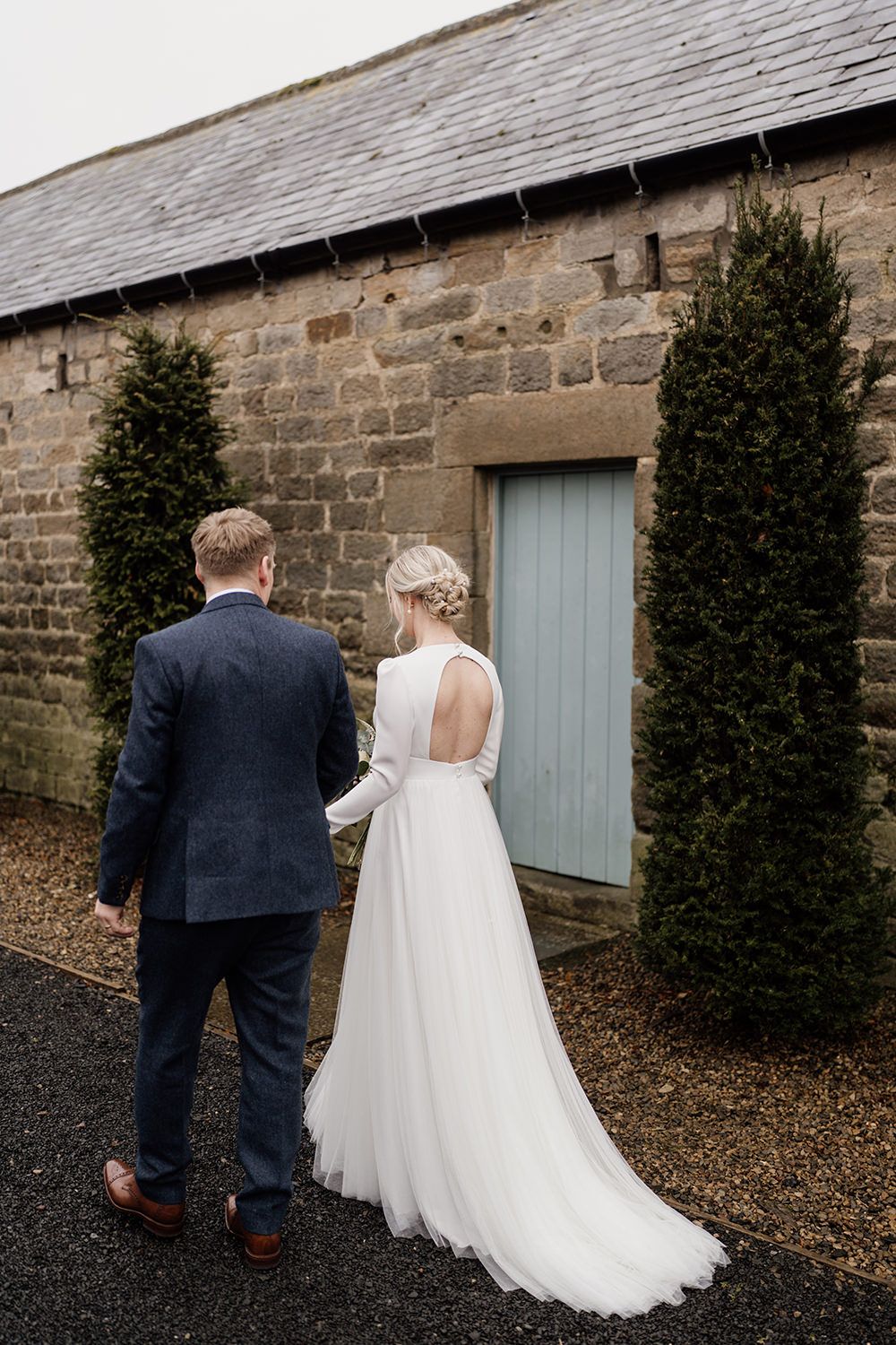 Bride and groom walking away from camera while holding hands.