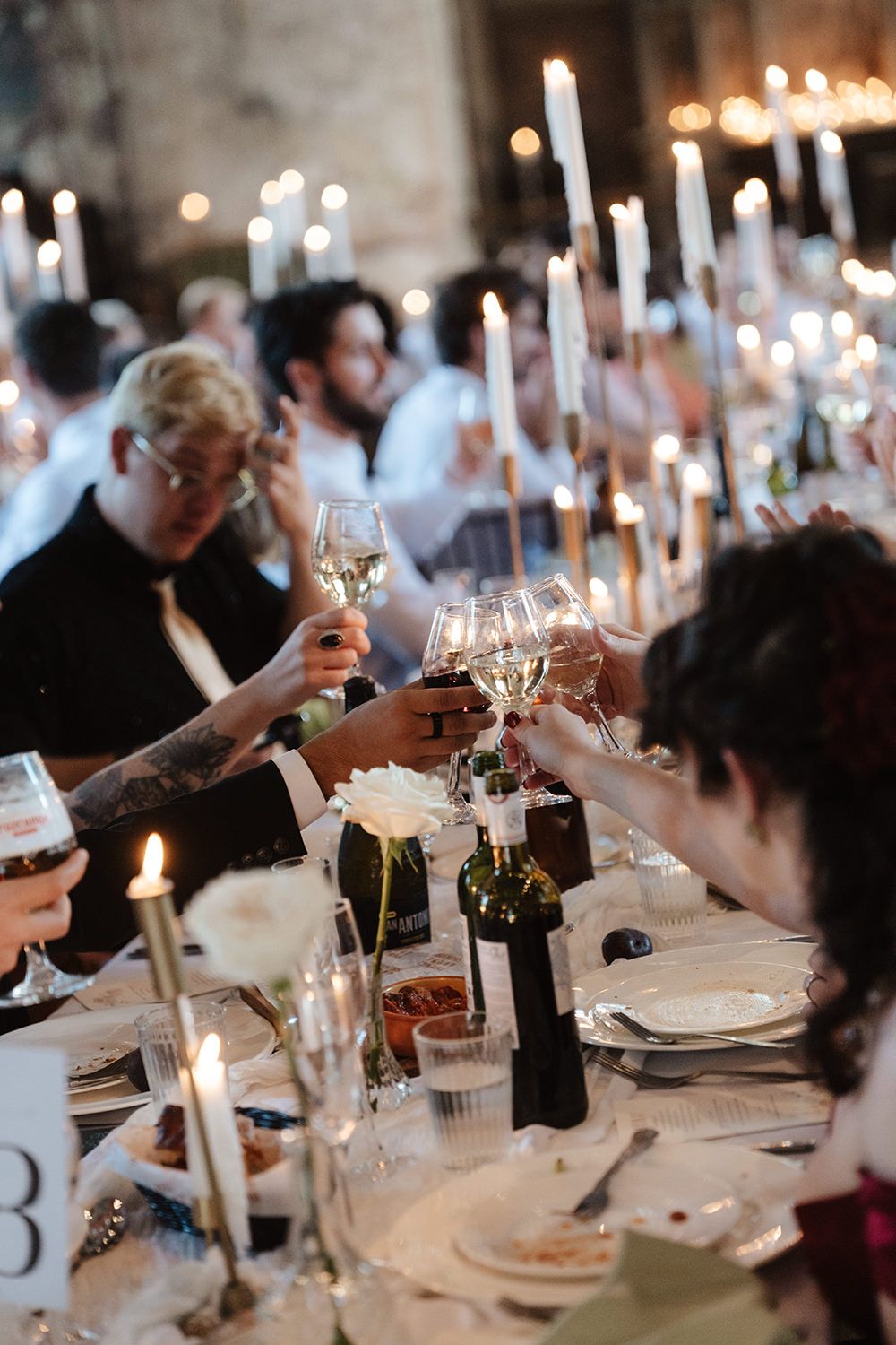 An elegant candlelit dinner reception with long tables set with wine glasses and white tapers.