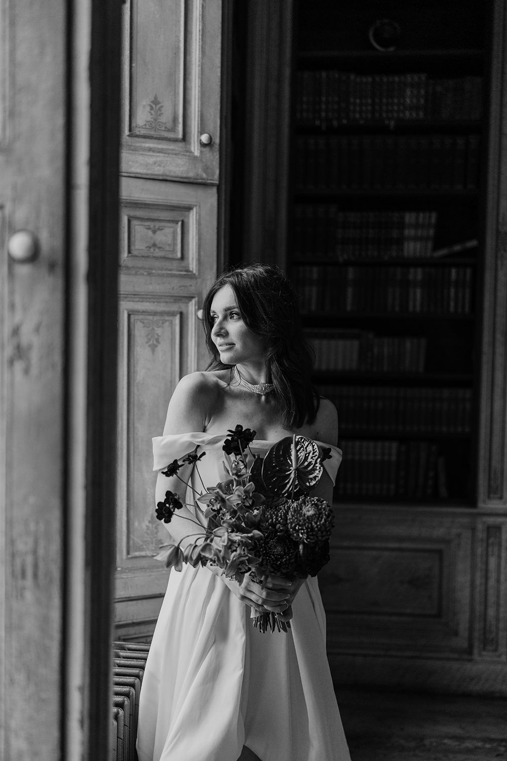 Solo portrait of a bride on her wedding day, while holding her autumnal flowers and looking out of the window.