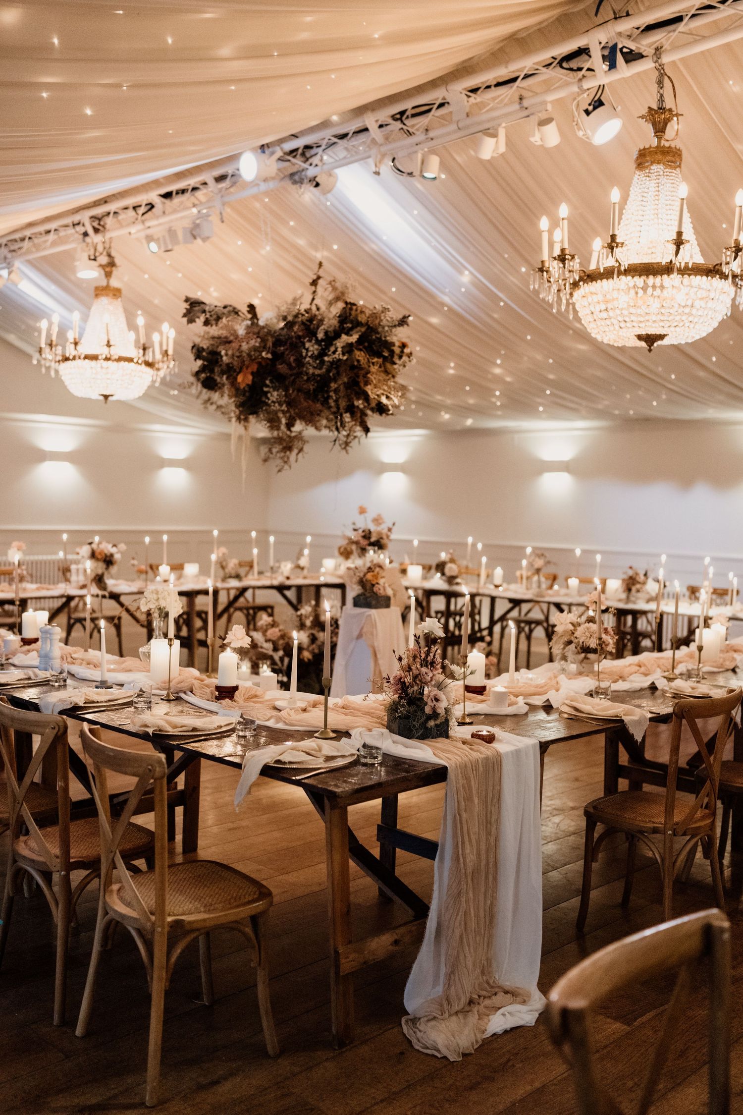 Elegant wedding reception venue with crystal chandeliers, farmhouse tables and ethereal white draping.