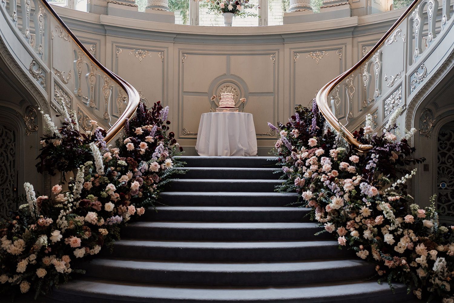 Elegant black staircase adorned with blush pink and white floral arrangements leading to a curved white backdrop.
