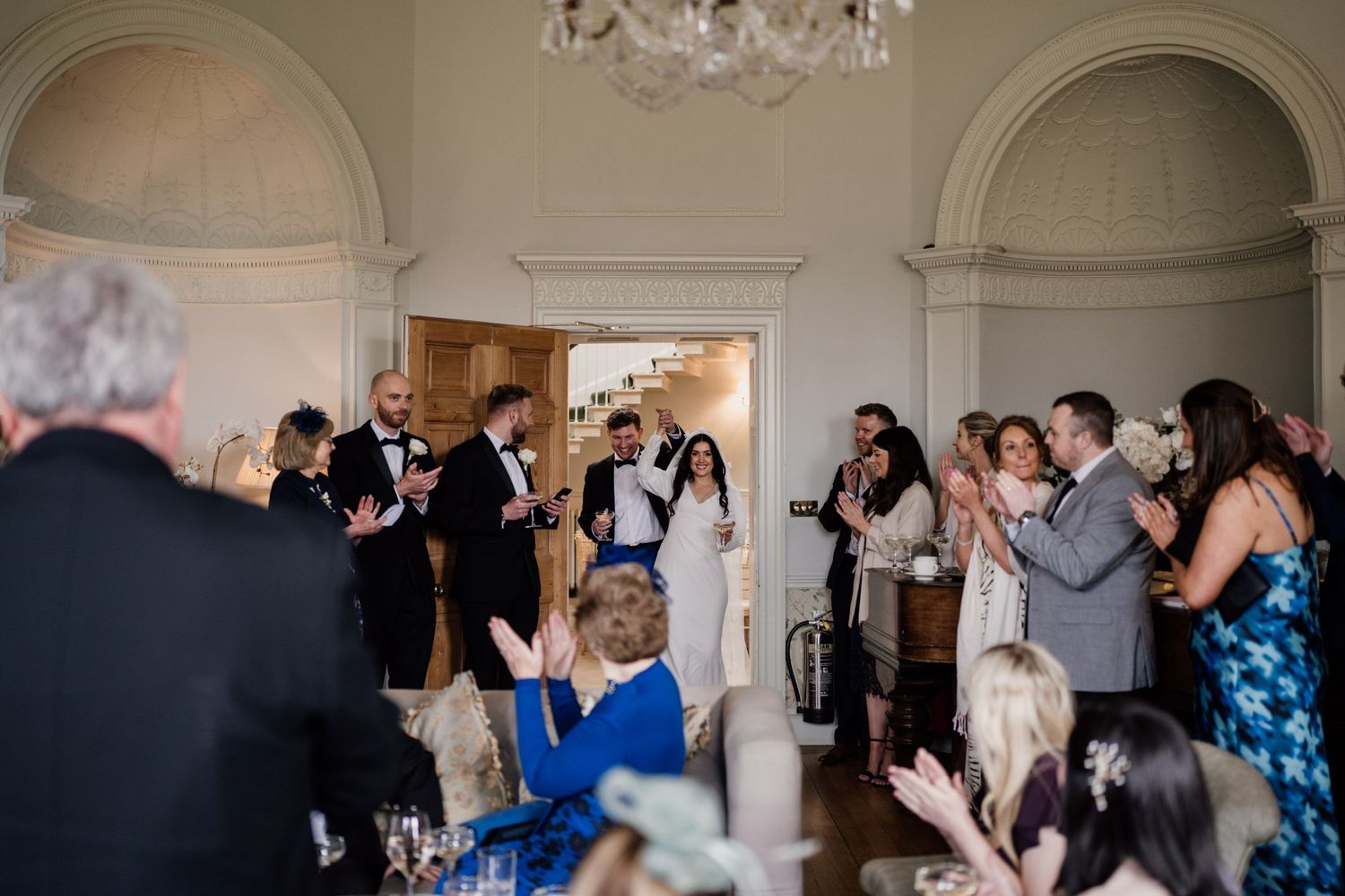 Bride and groom walking into a room filled with family and friends at Middleton Lodge Estate.
