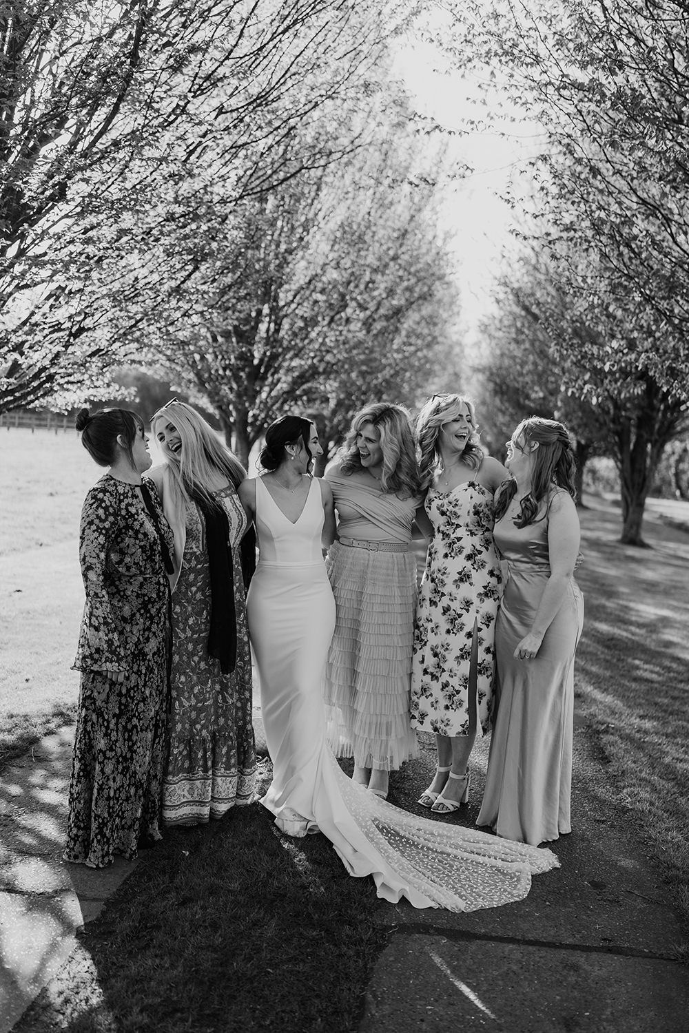 Bride and friends stood laughing in front of trees.