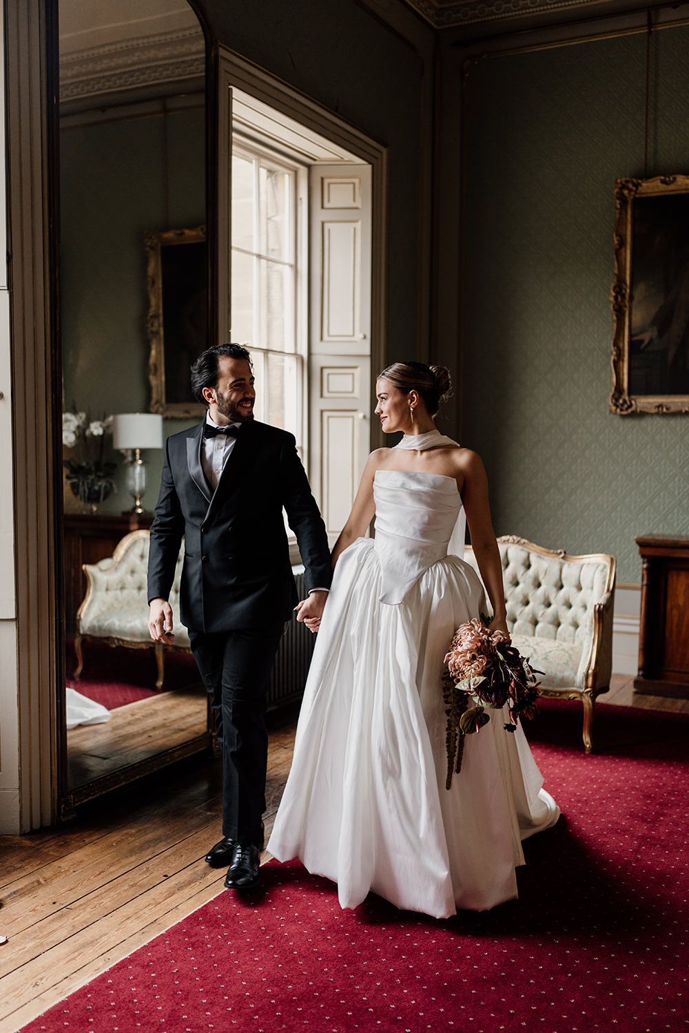 Editorial wedding portrait session: Bride and groom holding hands while looking towards each other.