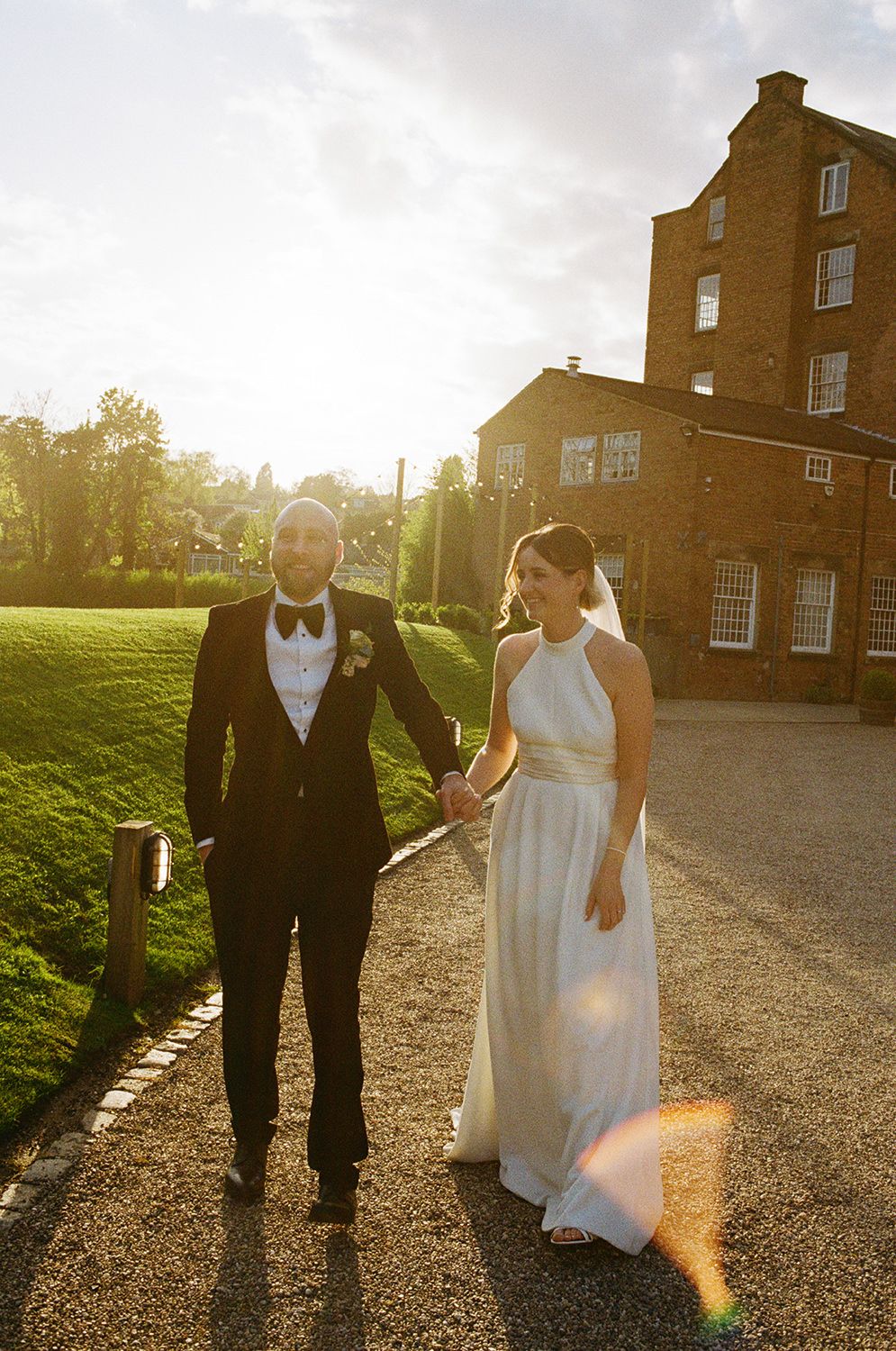 Bride and groom walking and laughing at sunset with The West Mill and River Derwent behind them.