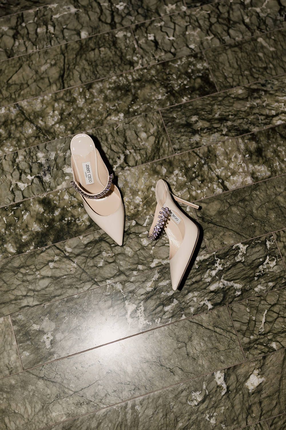 A pair of pale pink pointed kitten heels placed on a dark textured stone surface.