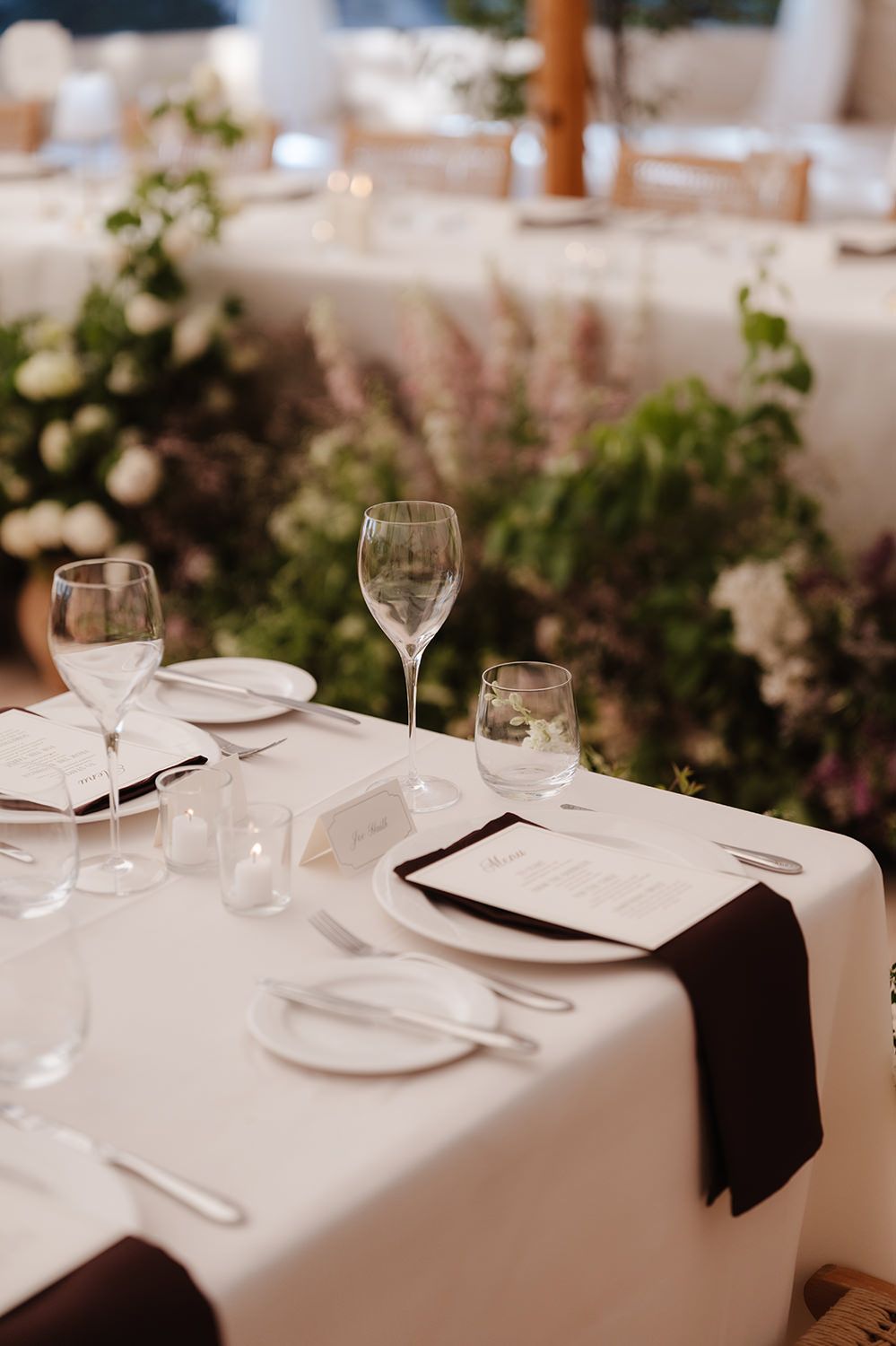 Elegant restaurant place settings with white tablecloths, wine glasses, and black napkins in a romantic, dimly lit setting.