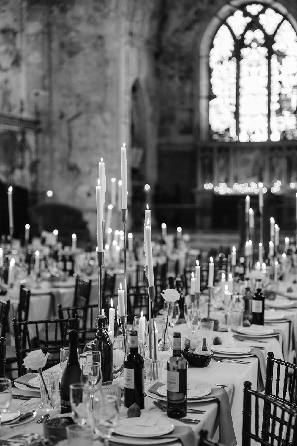 Elegant black and white wedding reception table setting with tall candles and place settings in a historic venue.