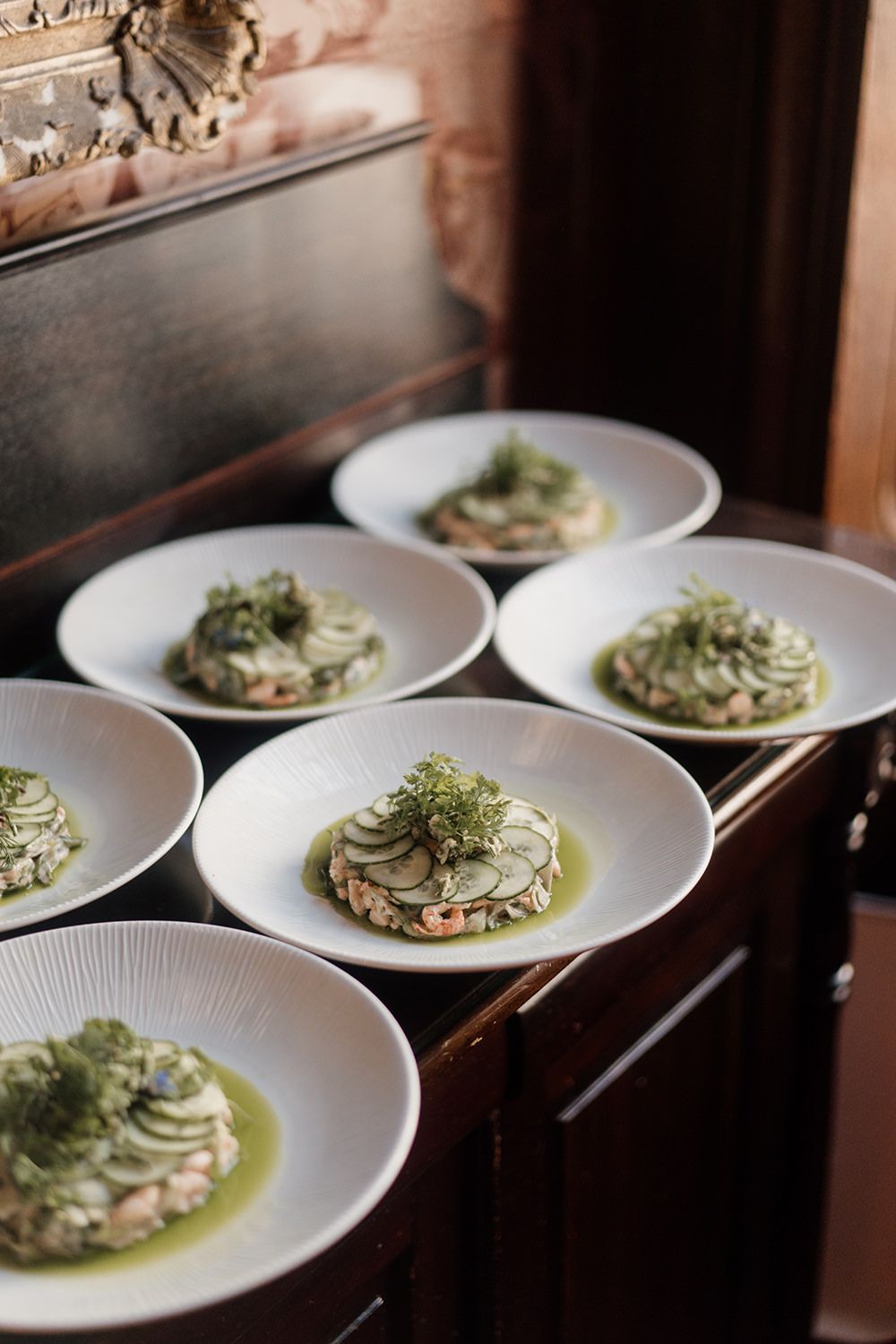 Multiple white plates of elegantly plated appetizers with microgreens garnish on a dark wooden surface.