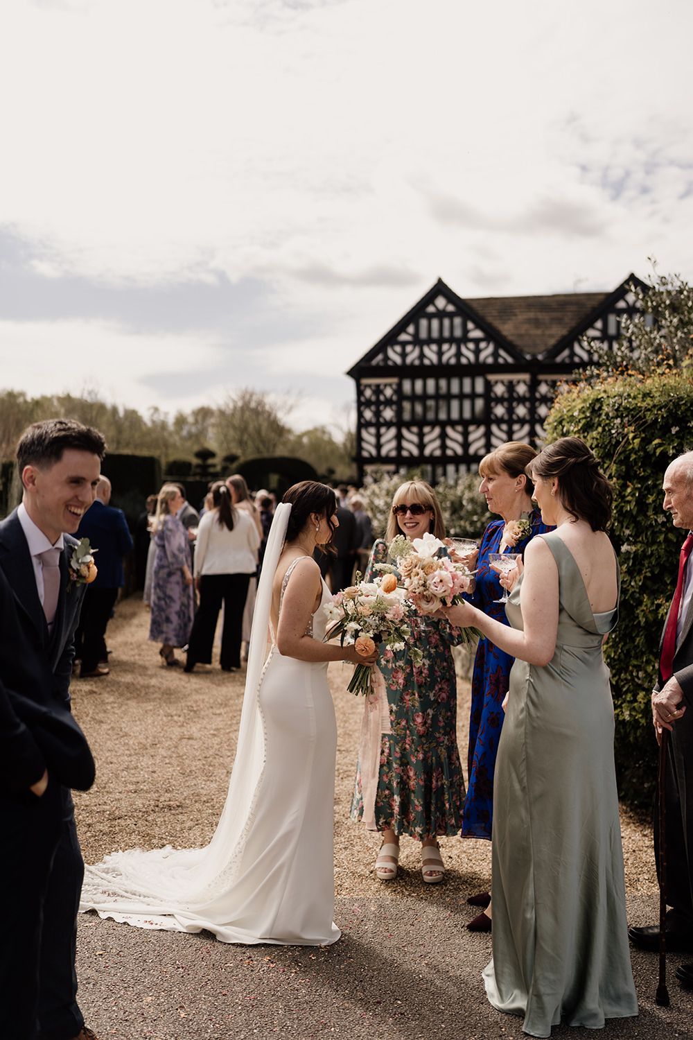 Bride talking to wedding guests on wedding day with Holford Hall in the background.
