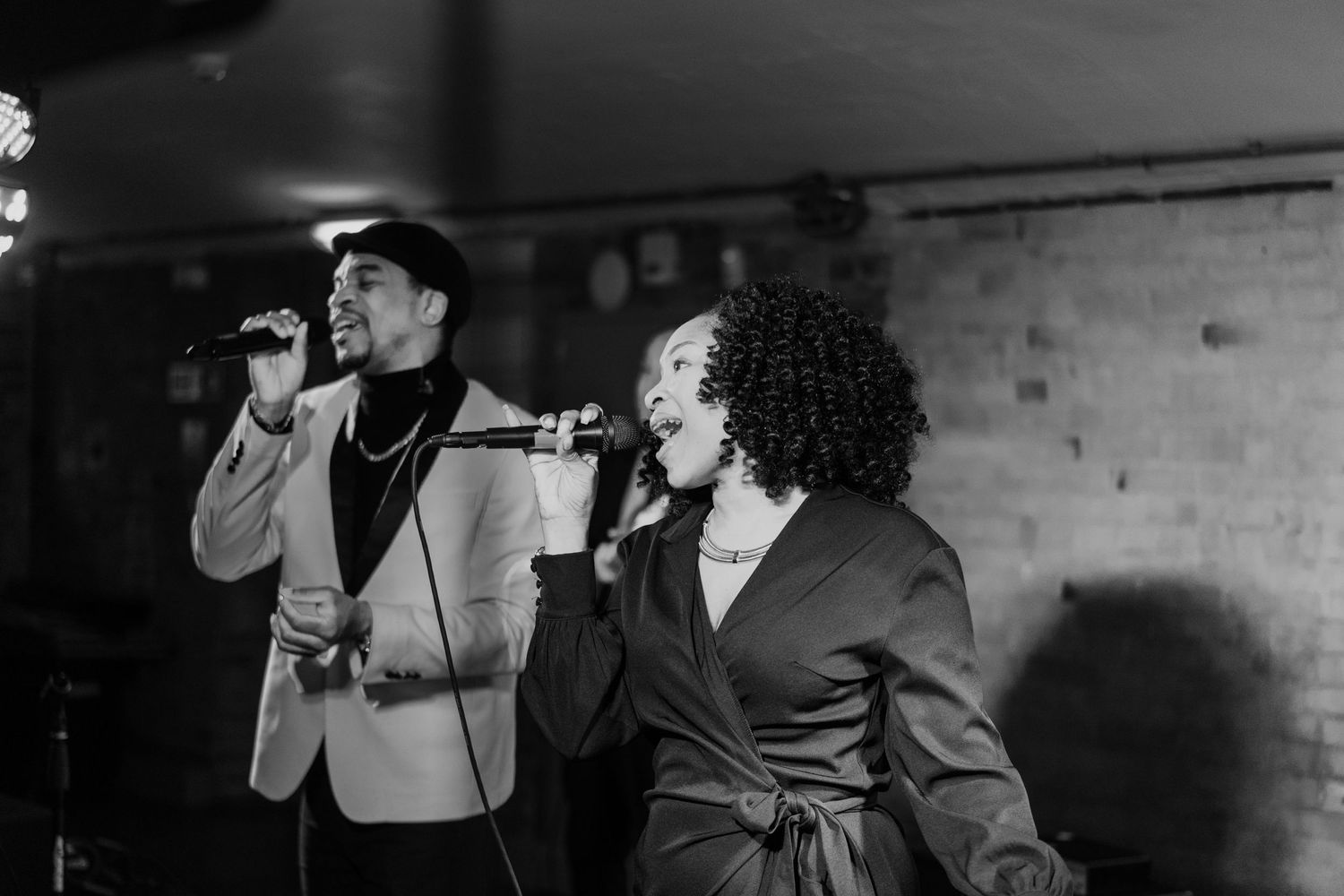Two performers sing passionately on stage at a wedding reception in black and white.