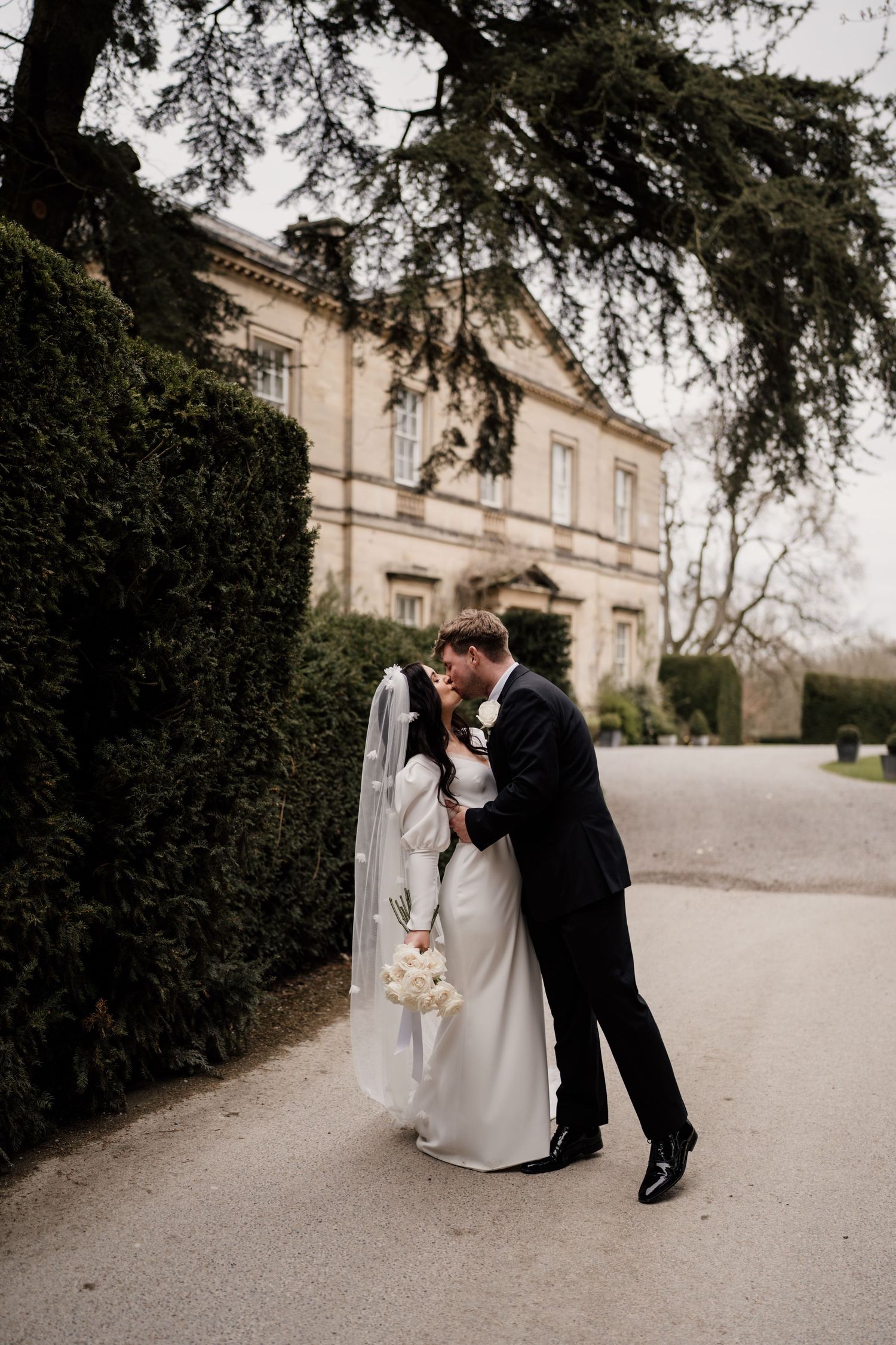 Bride and groom kissing with the main house at Middleton Lodge Estate behind.