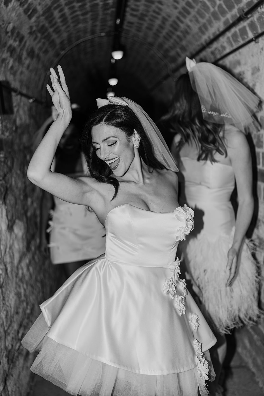 A series of black and white photos showing a bride in a white dress dancing joyfully in what appears to be a brick tunnel.