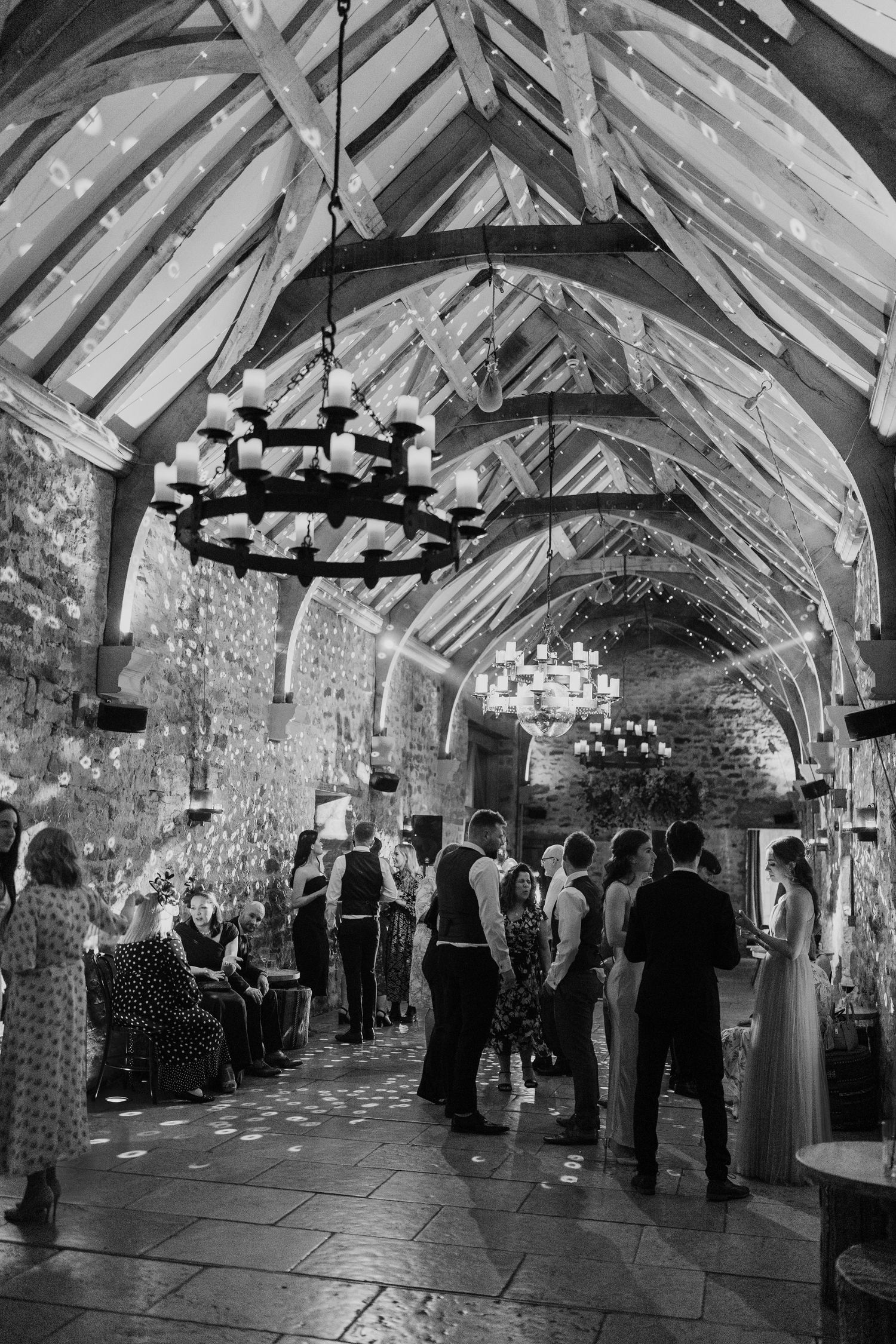 Black and white photos of a rustic barn reception venue with exposed beams and chandeliers decorated for a wedding.