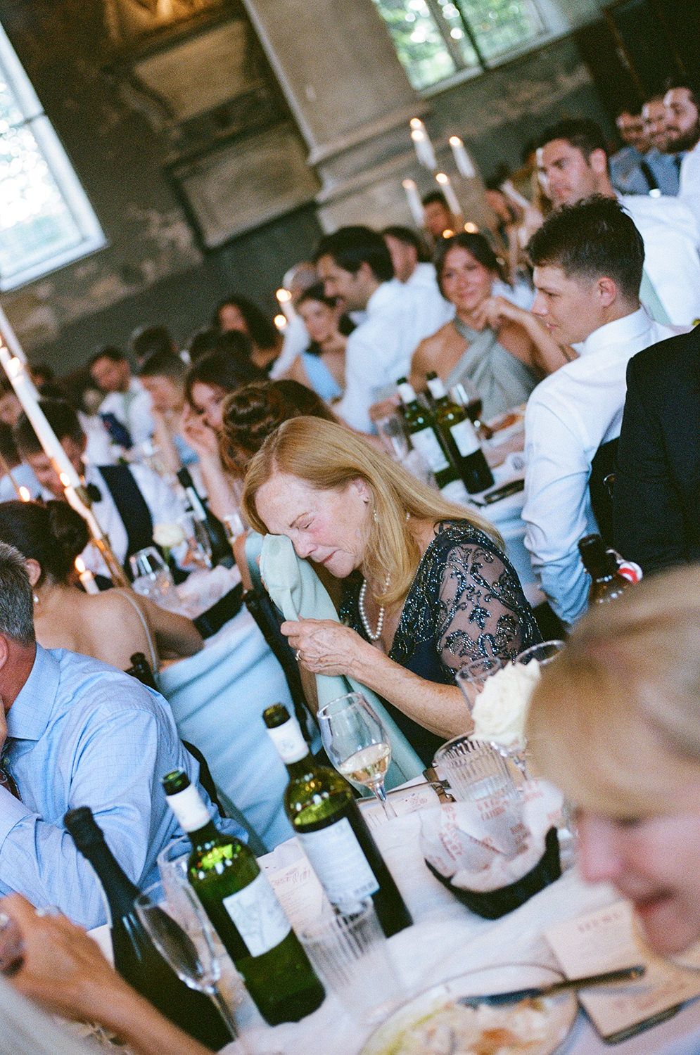 Guests enjoying a meal and wine at rustic wedding reception with candle centerpieces.