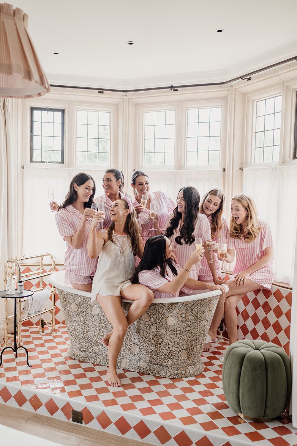 A group in pink and white striped pajamas gather around an ornate bathtub in a bathroom with checkered floor tiles.