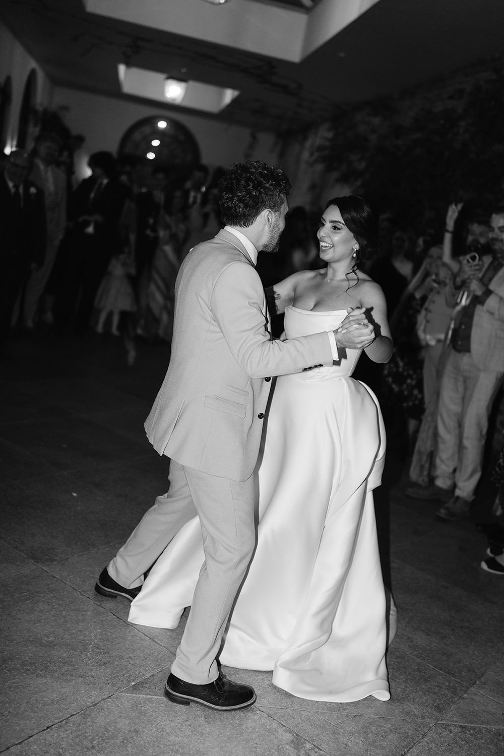 A couple shares their first dance at a wedding reception, with the bride wearing a stunning white strapless gown.