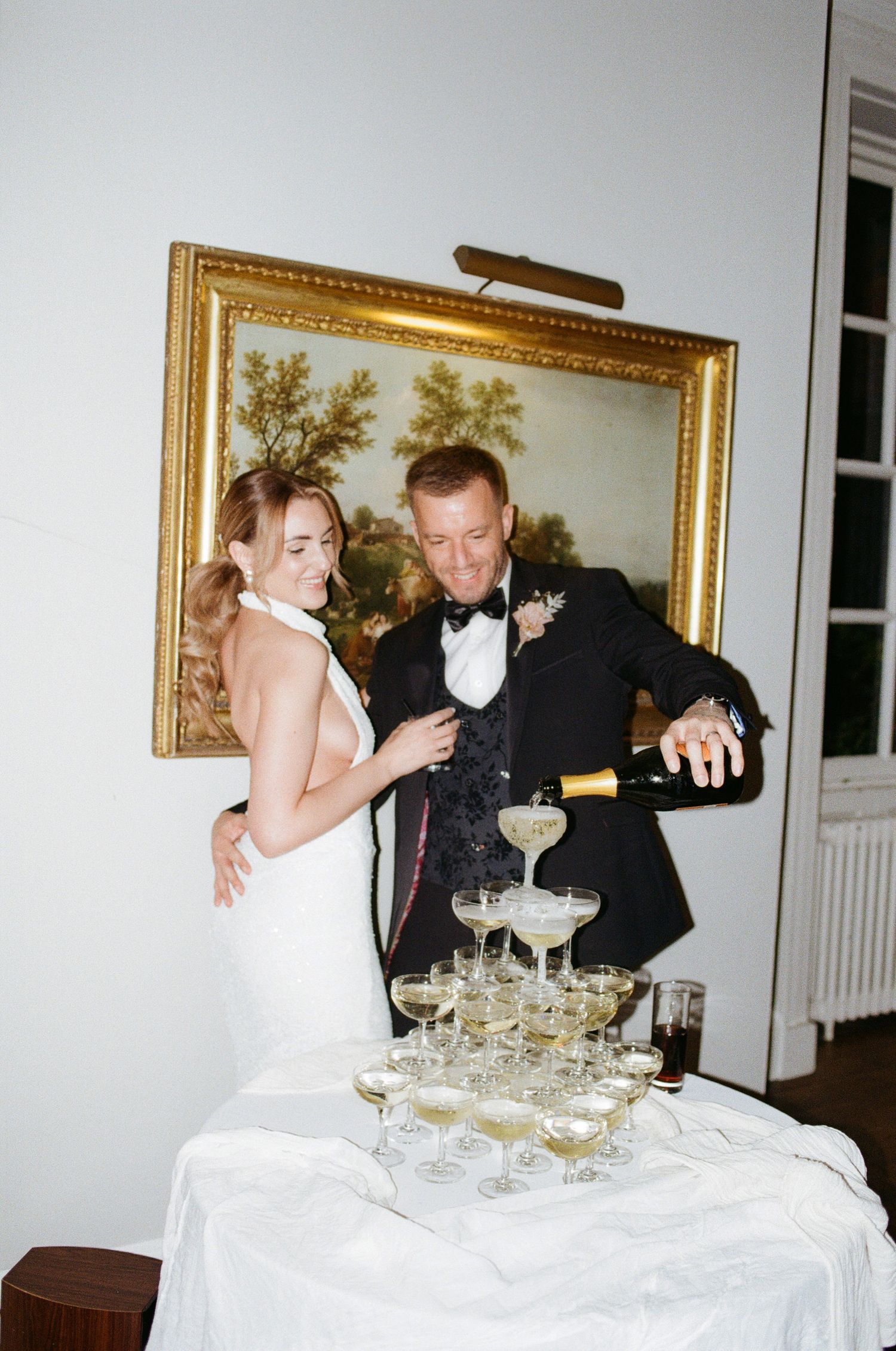 A couple pours champagne into a tower of glasses at an elegant celebration.