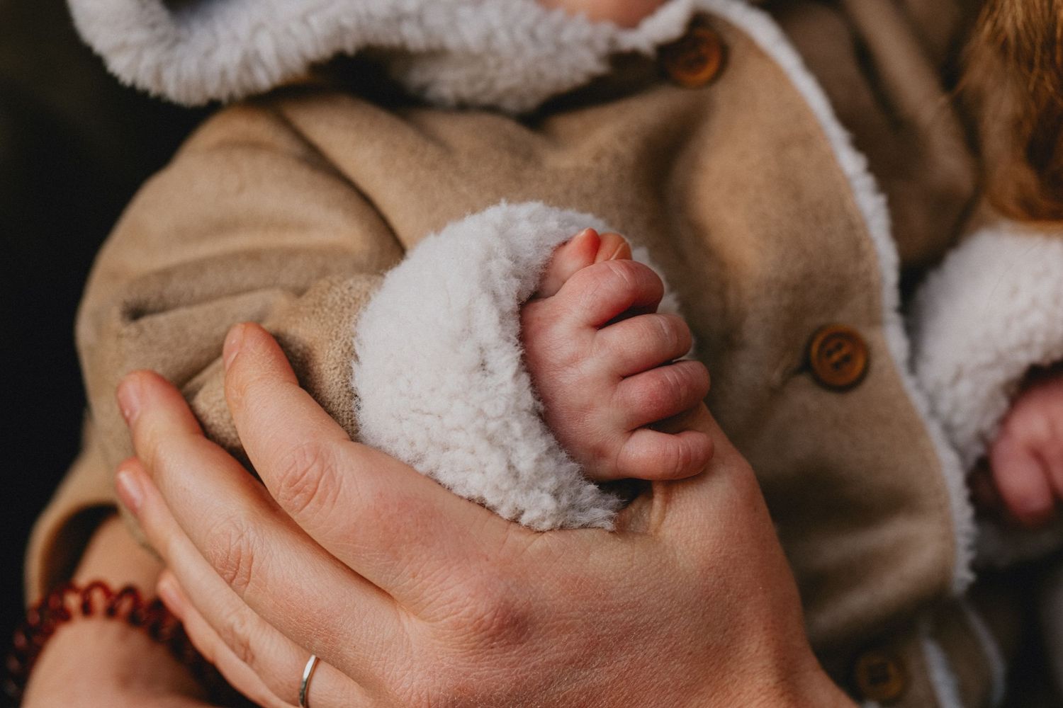 A tiny baby foot nestled in soft white sherpa fabric against a tan coat.