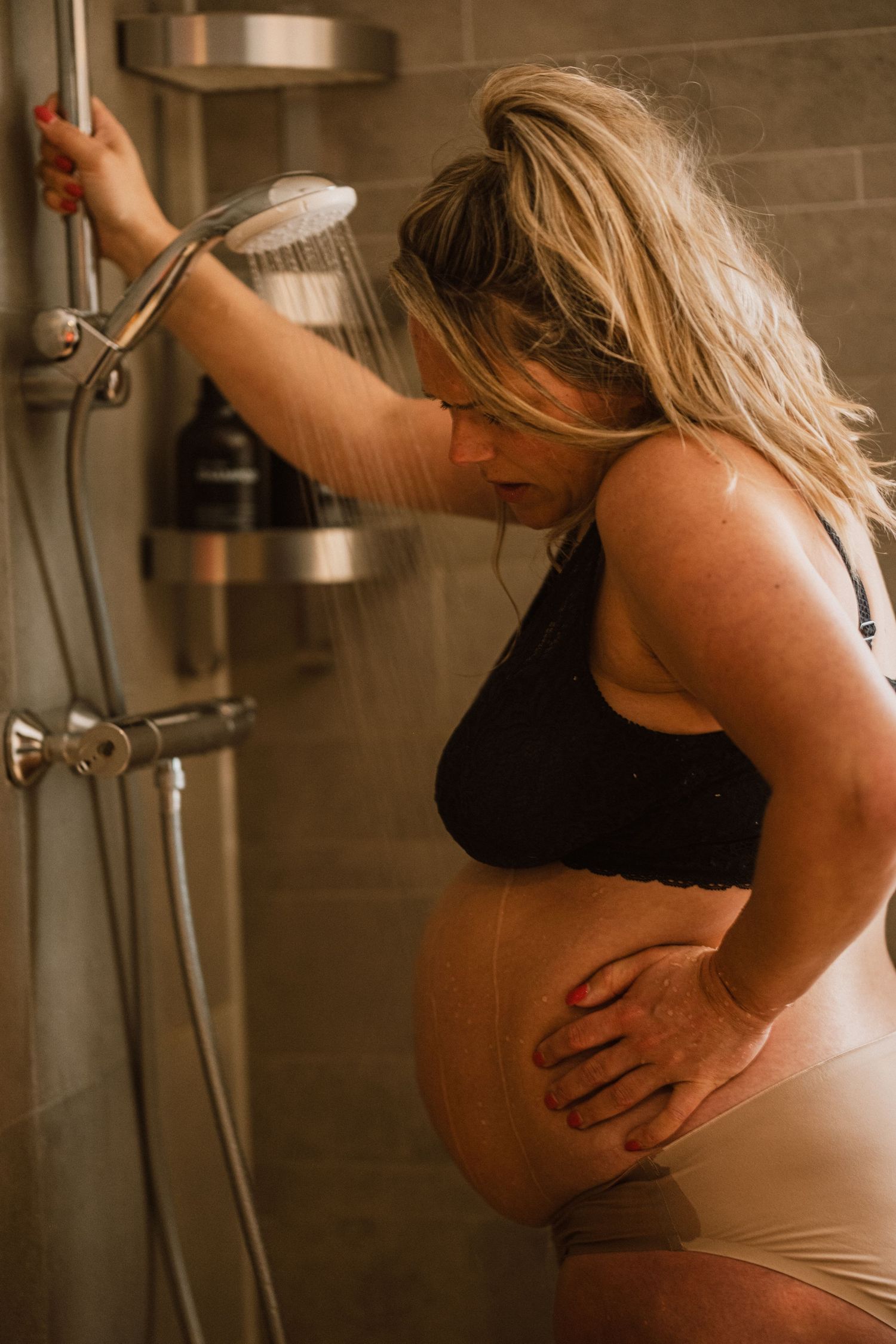 Vrouw vangt weeën op onder douche tijdens thuisbevalling, geboortefotografie Den Haag en Leiden door Mama Nora Fotografie