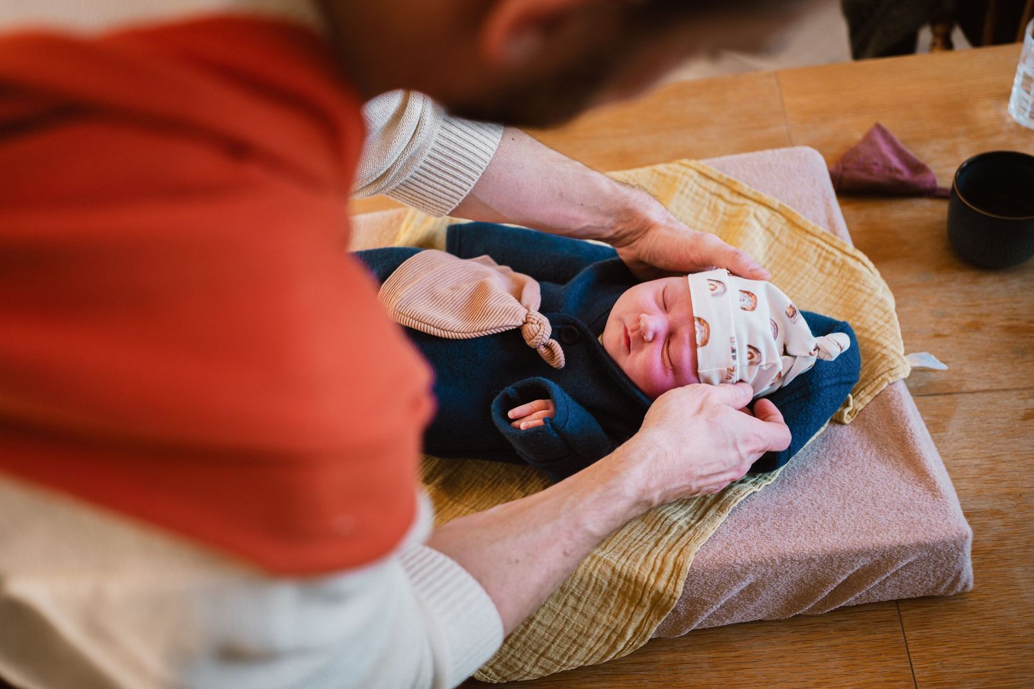 Parent dressing newborn baby in blue outfit on changing mat on wooden table.