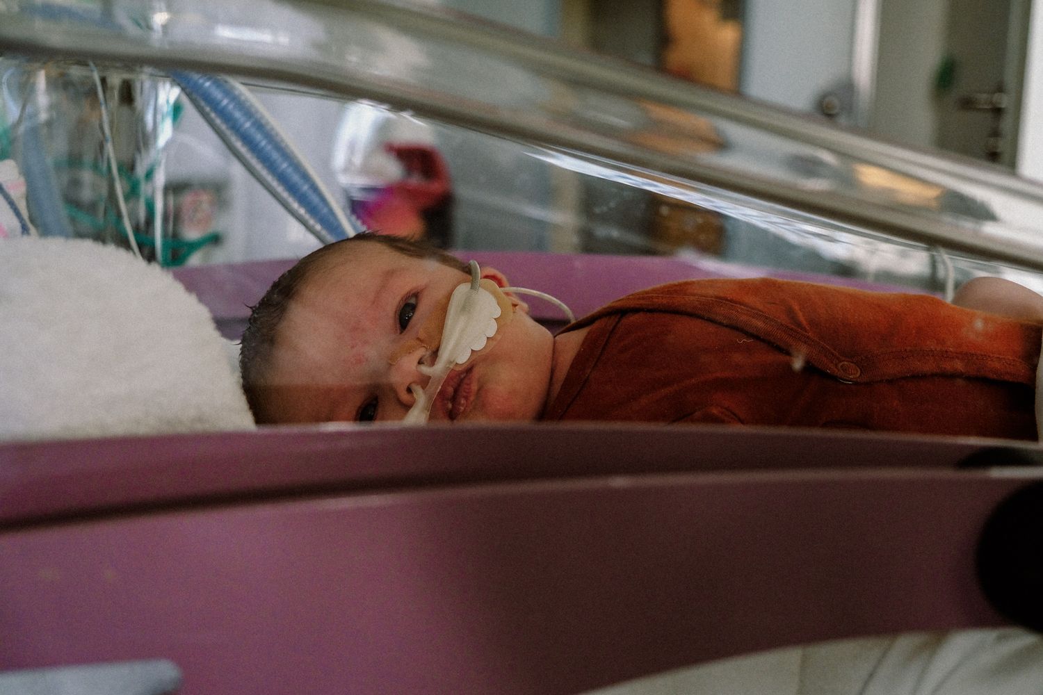 Premature newborn baby resting in a hospital incubator with medical tubes, wrapped in an orange blanket.