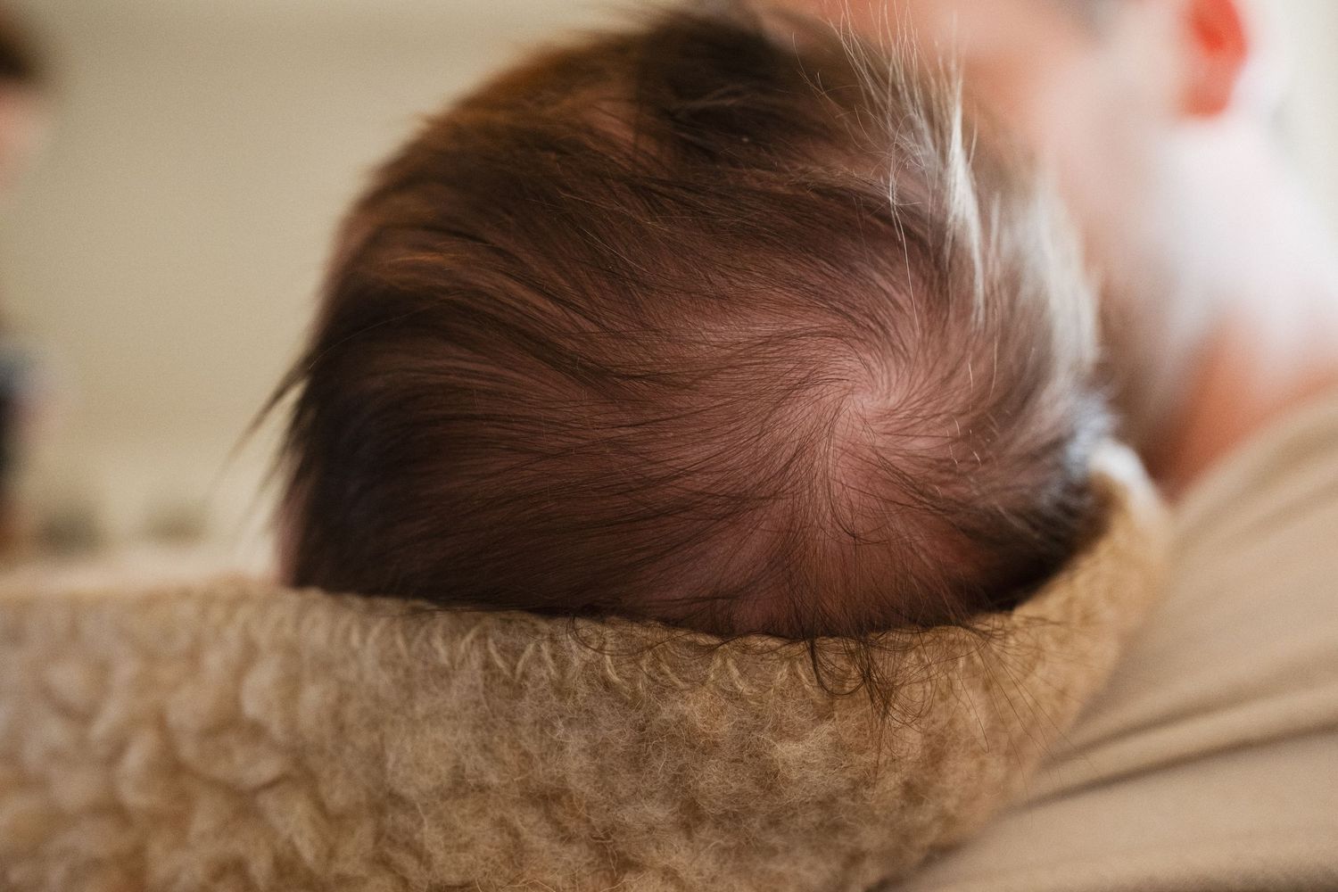 Close-up of a newborn baby's head with fine hair resting on a soft blanket.