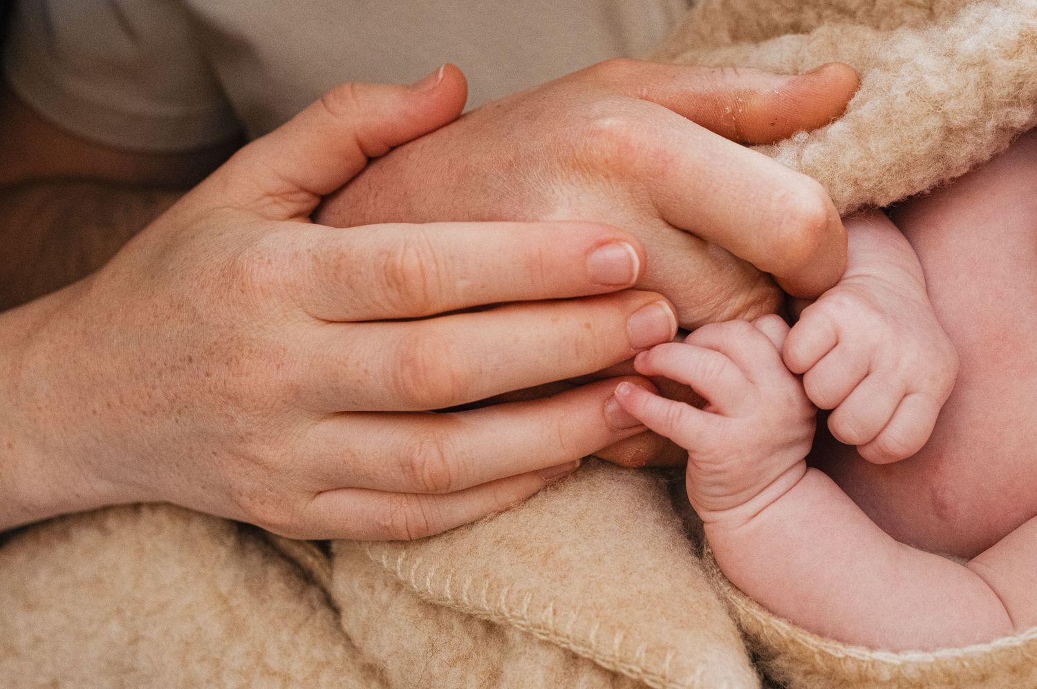 Adult hands tenderly cradling a newborn baby's feet wrapped in a soft blanket.