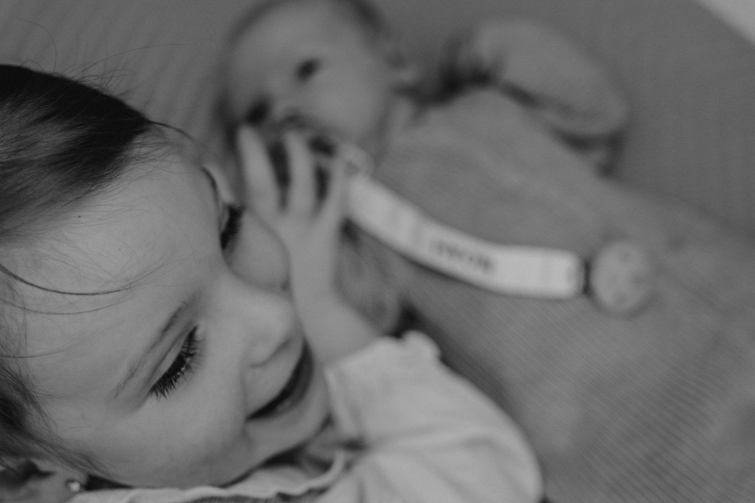 Black and white photo of a young toddler smiling while holding a baby doll in a crib.