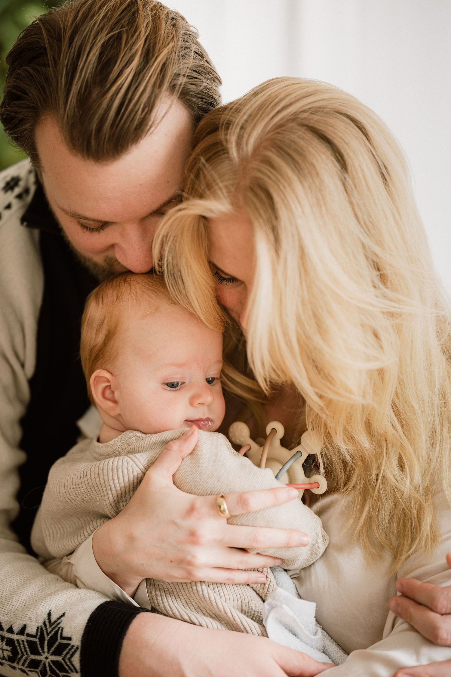 Parents lovingly kiss their newborn baby, captured in a warm and tender family portrait photo.